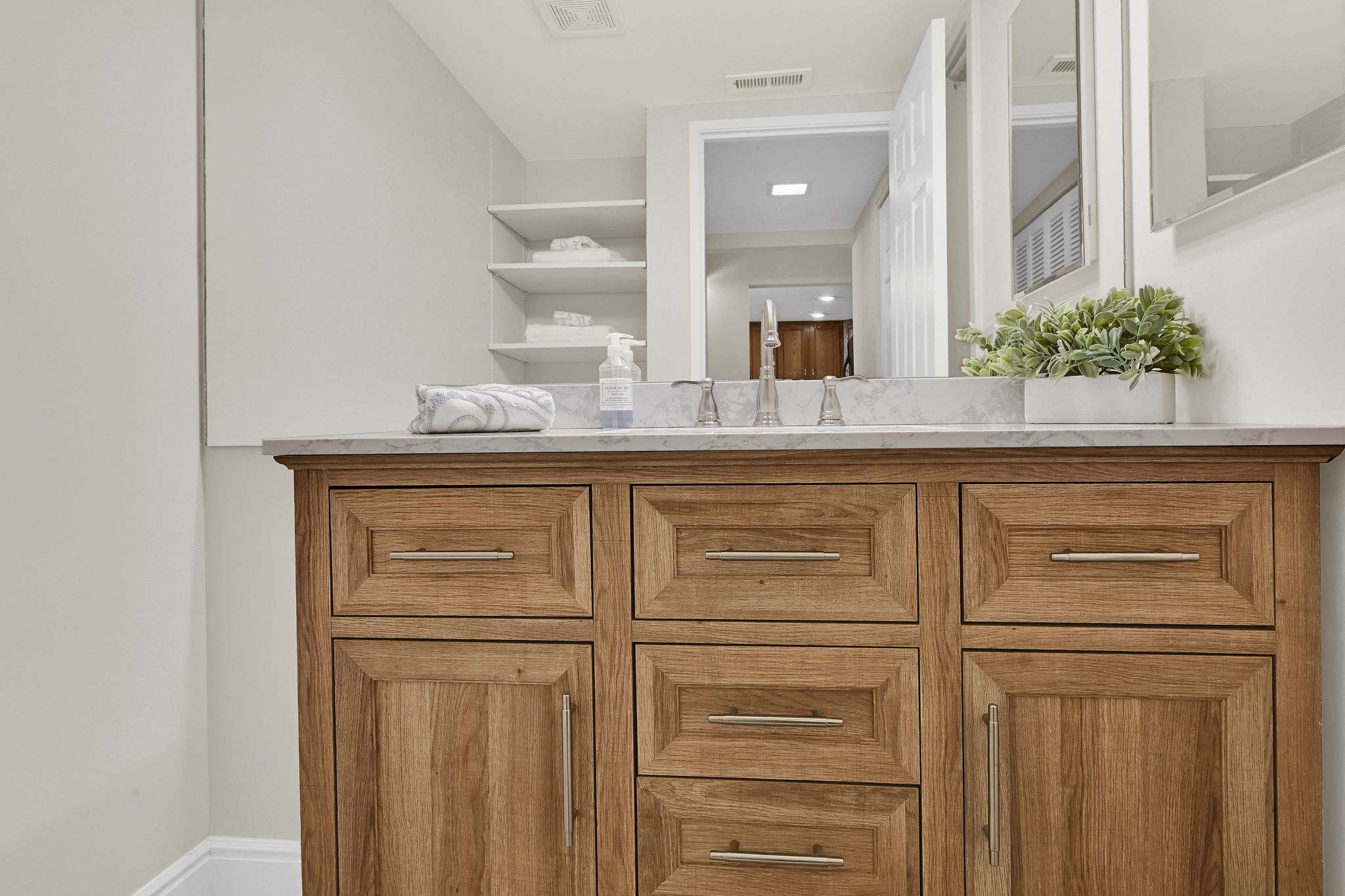 Wood-finish vanity with a light-toned countertop, brushed nickel hardware, and built-in shelving