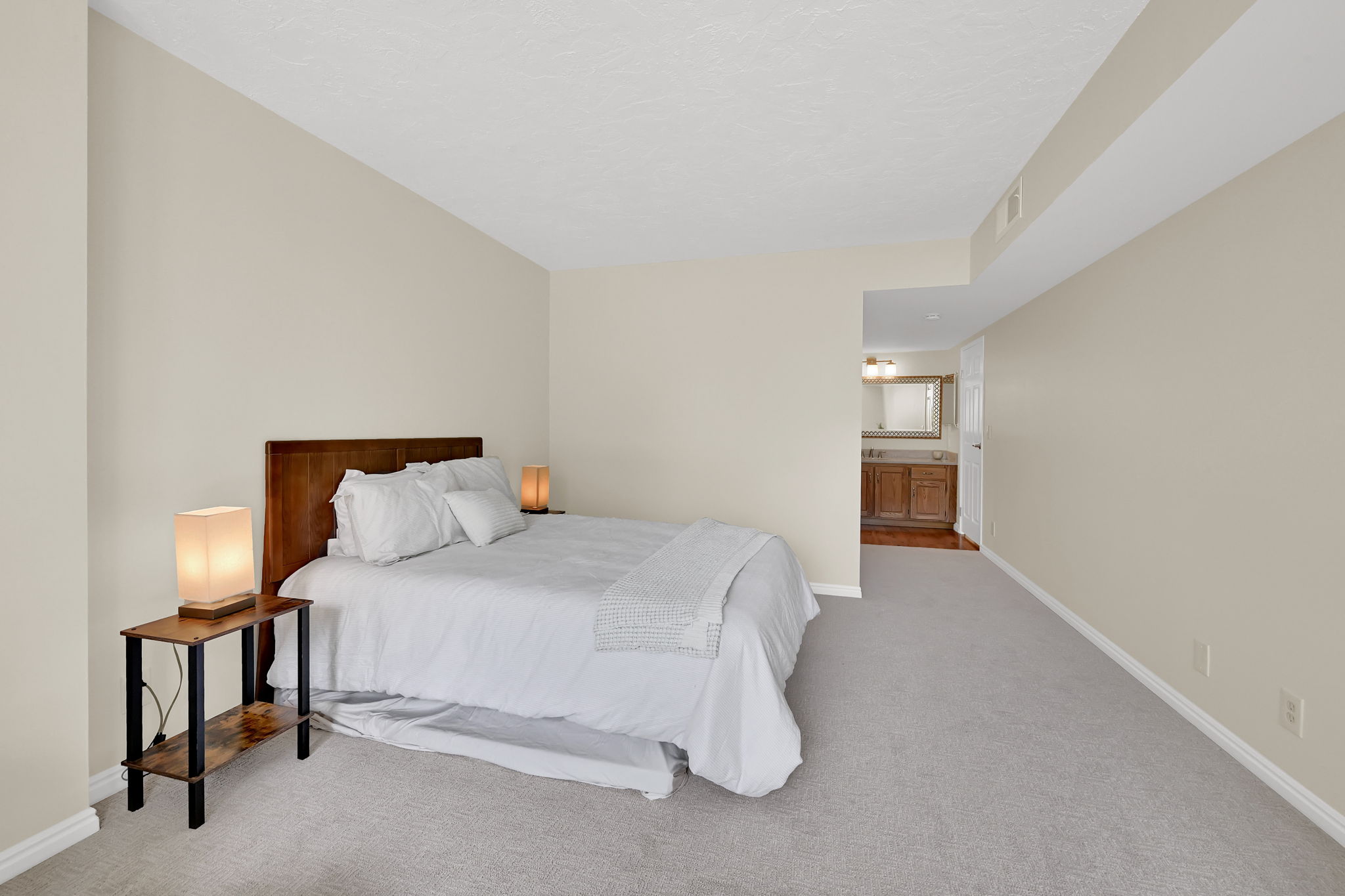Spacious bedroom featuring light-colored carpet, neutral wall paint, and a wood headboard