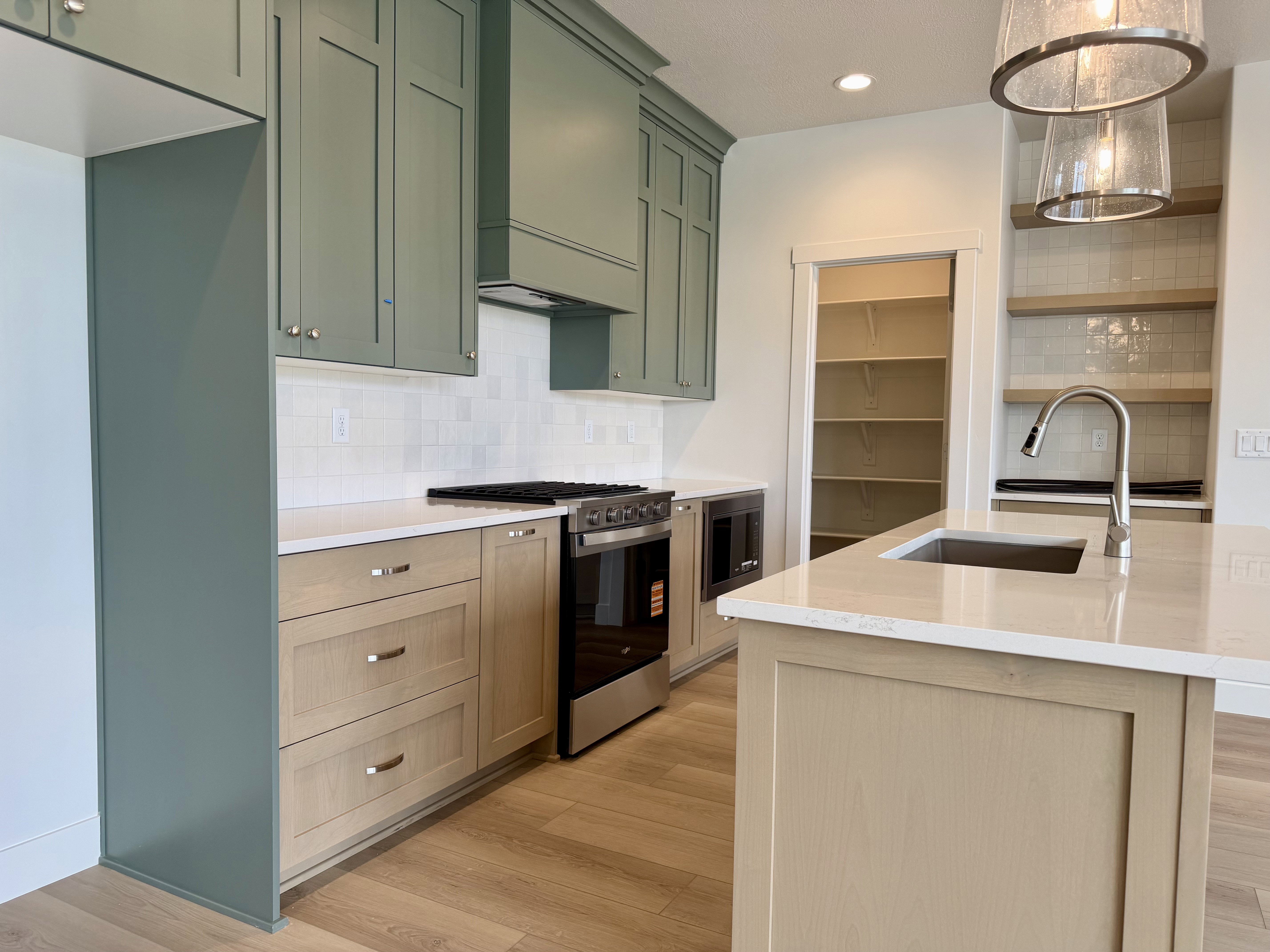 Modern kitchen featuring light green upper cabinetry and natural wood-finish lower cabinetry, complemented by a white subway tile backsplash