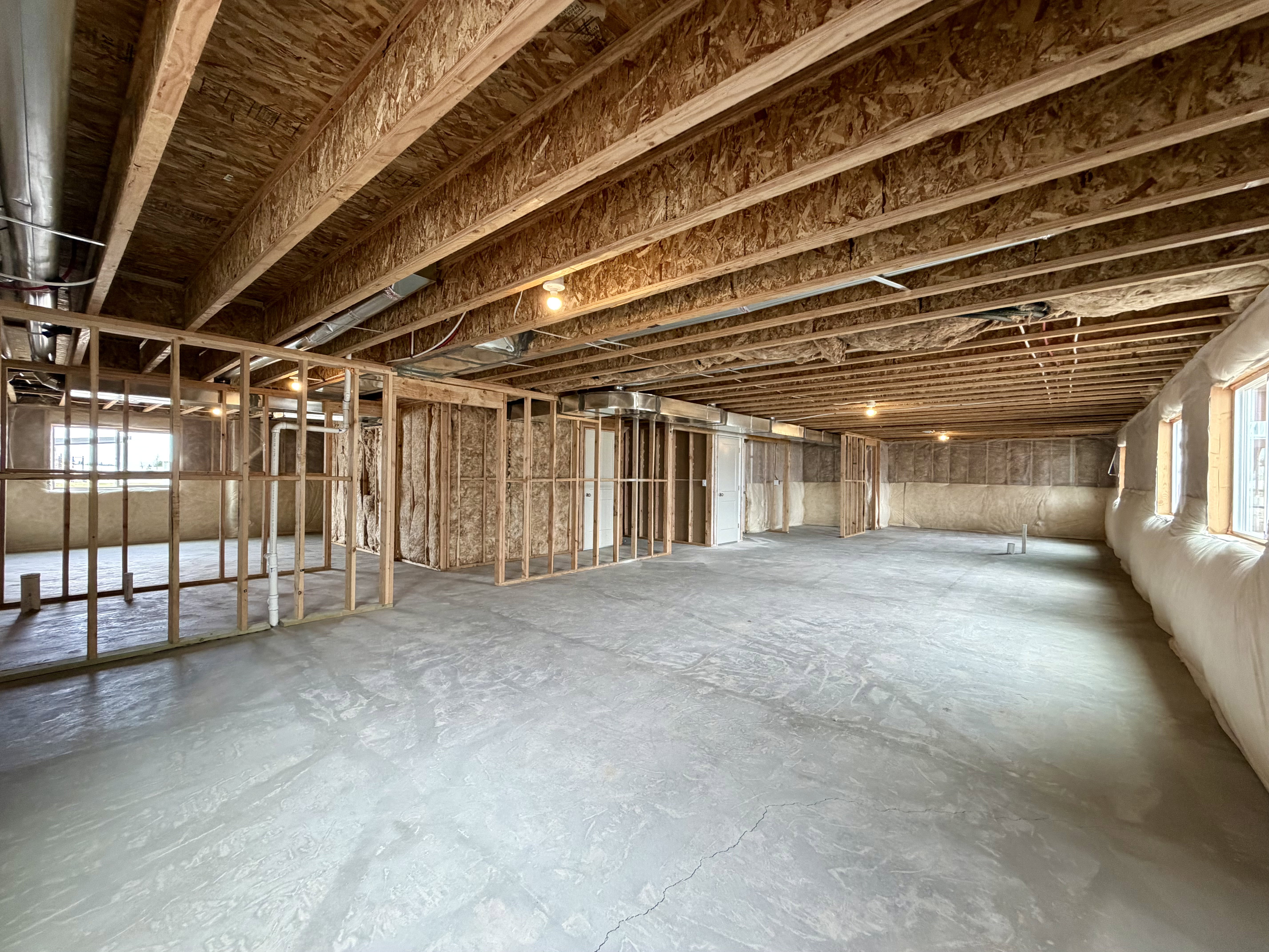 Spacious unfinished lower level featuring exposed ceiling joists, concrete flooring, framed wall sections, and multiple window openings