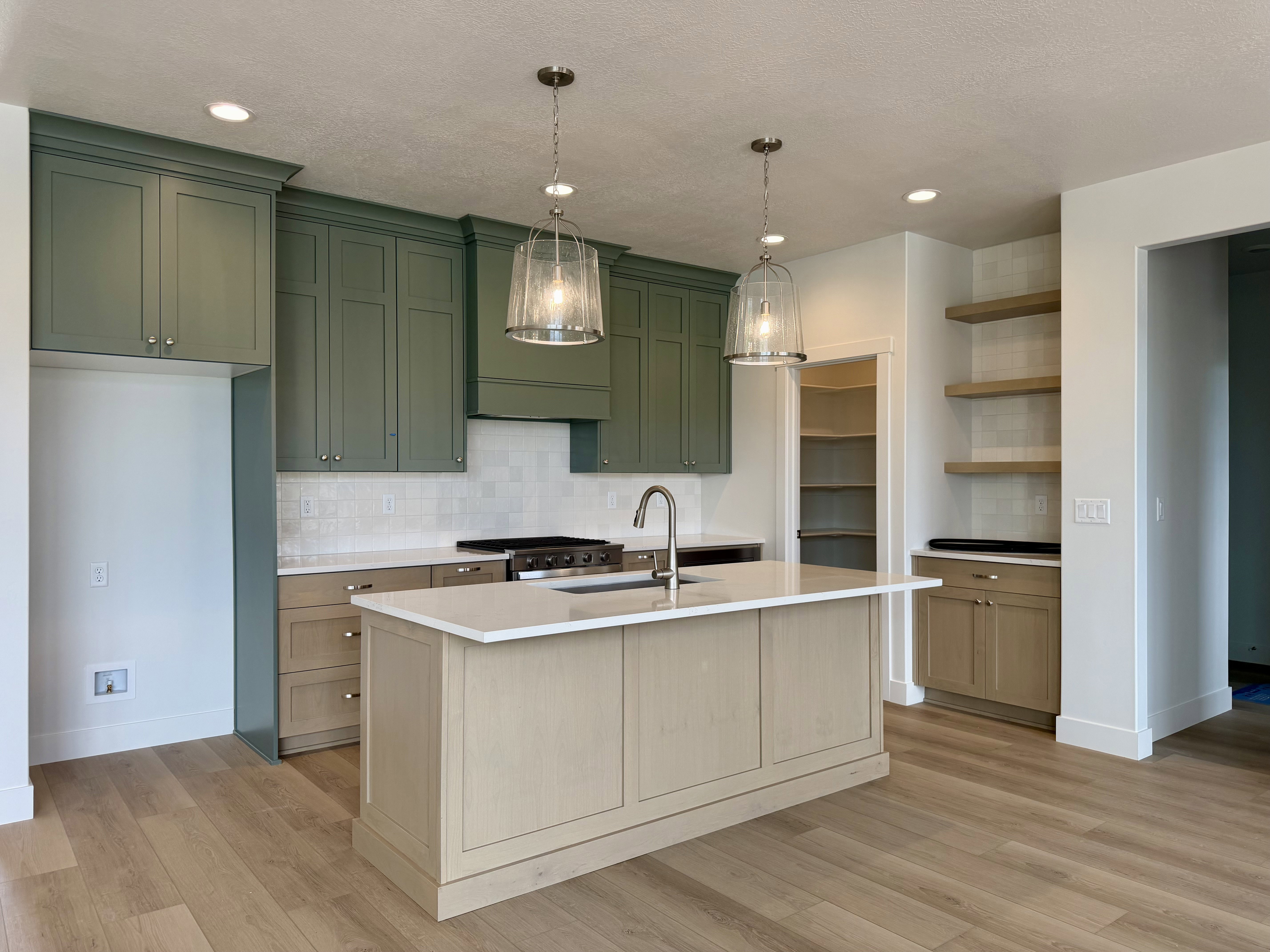 Kitchen featuring a central island with an undermount sink, quartz countertops, a gas range with a custom hood, light green upper cabinetry, and light wood-finish lower cabinetry