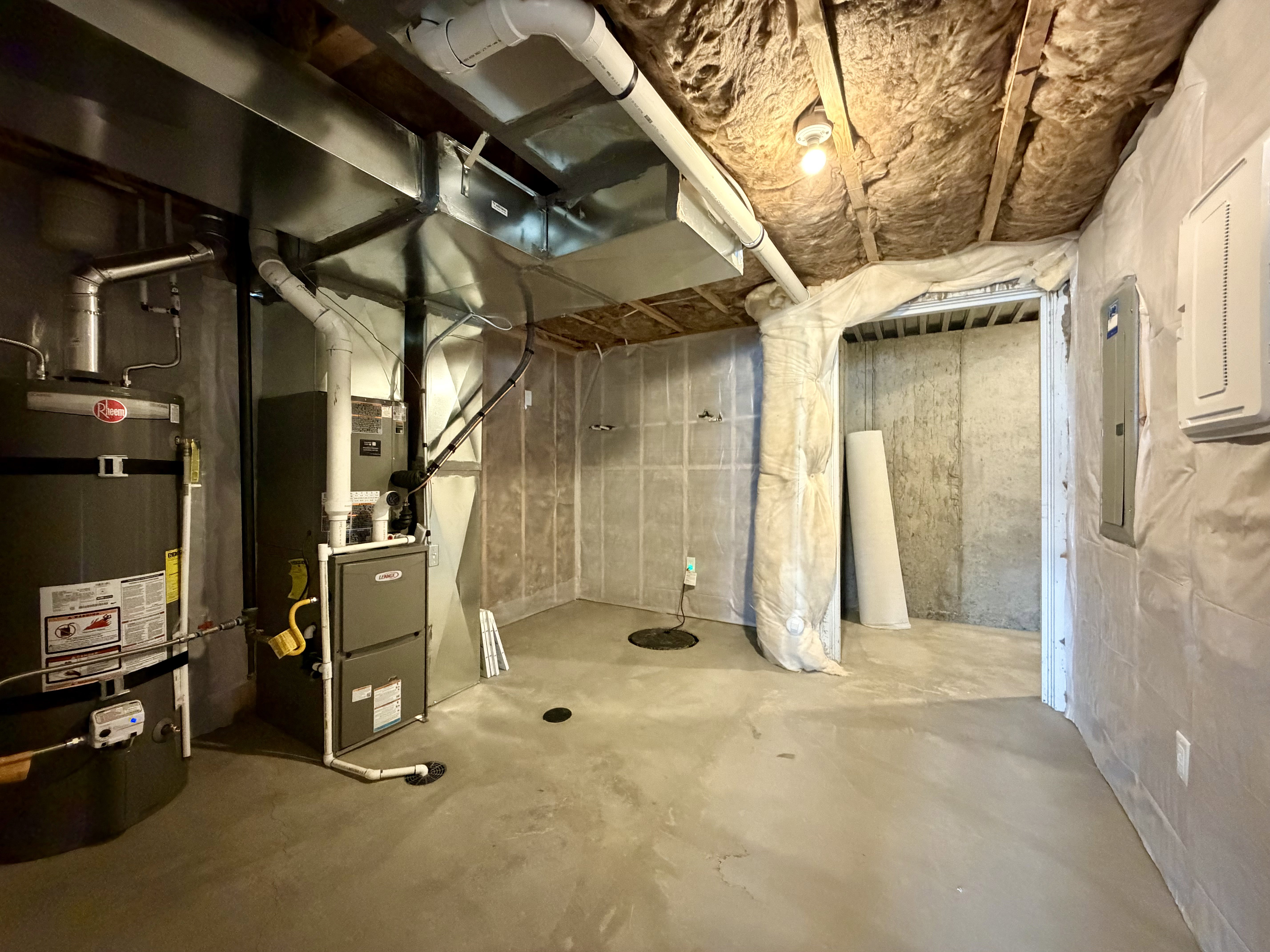 Unfinished basement featuring a concrete floor, exposed joists with insulation, a water heater, a furnace, and a sump pump
