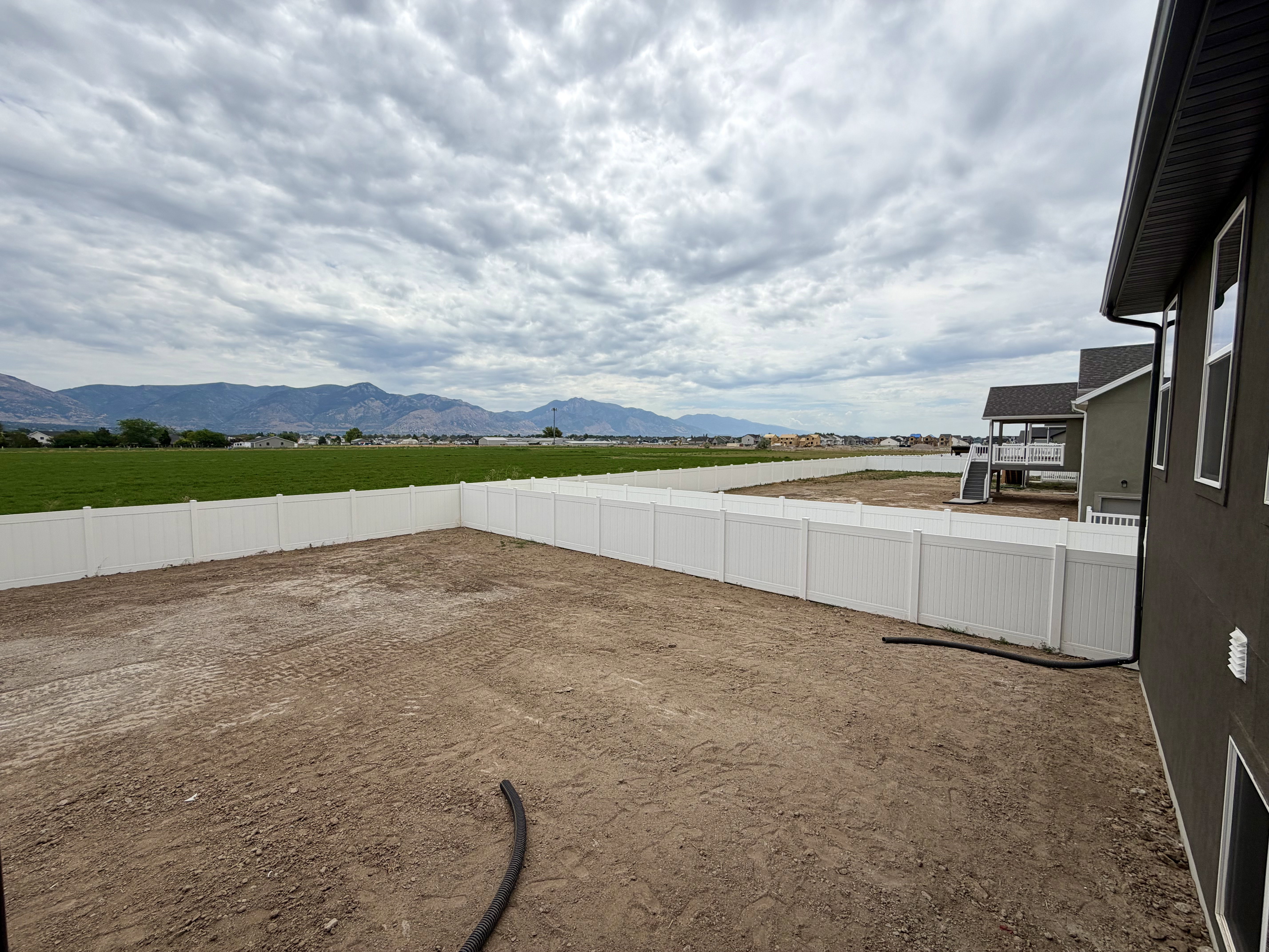 Spacious backyard featuring a new vinyl privacy fence, dark gray exterior siding, and distant mountain scenery