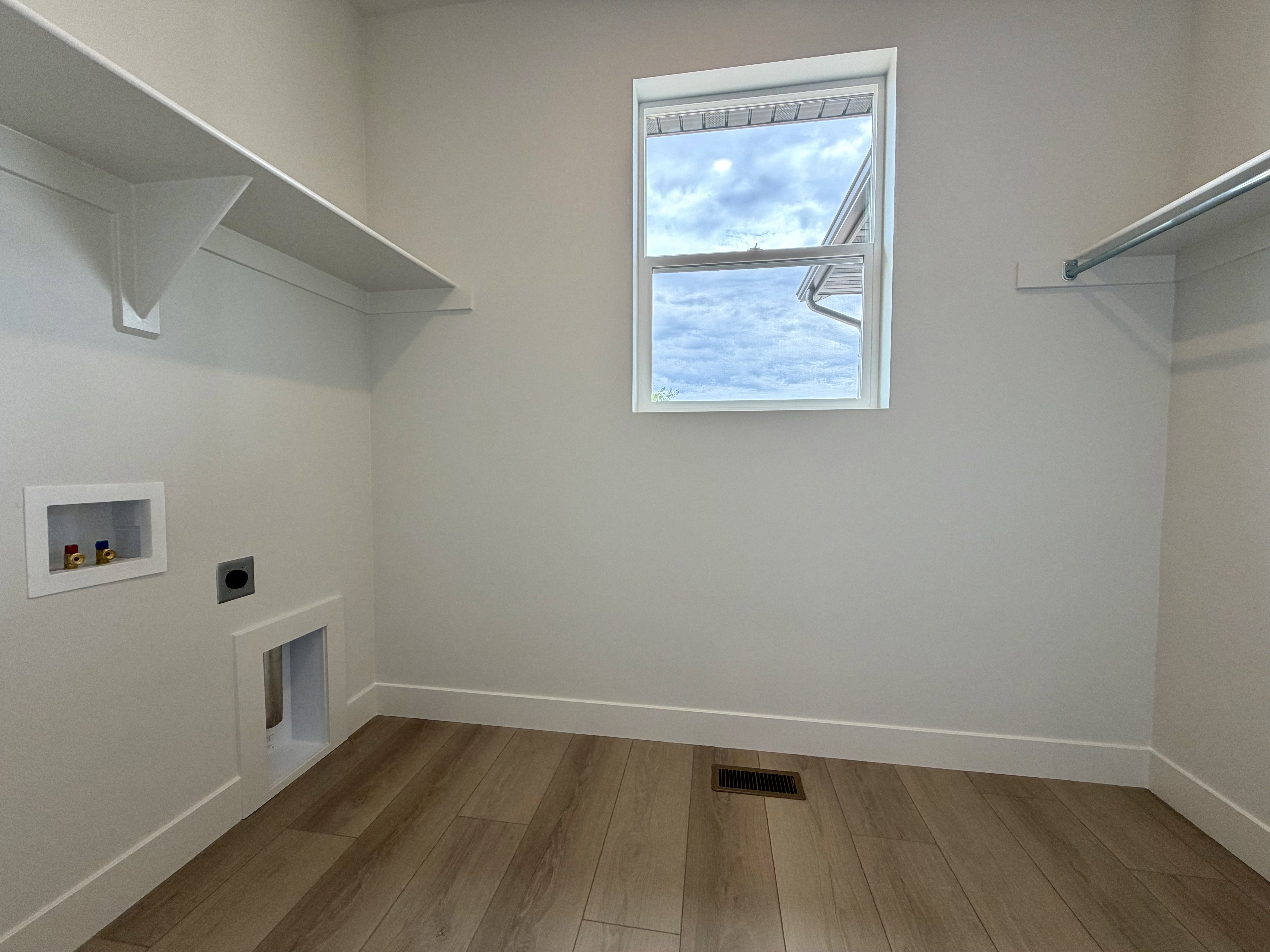 Utility room featuring wood-finish flooring, a window, and white shelving with an integrated clothes hanging rod