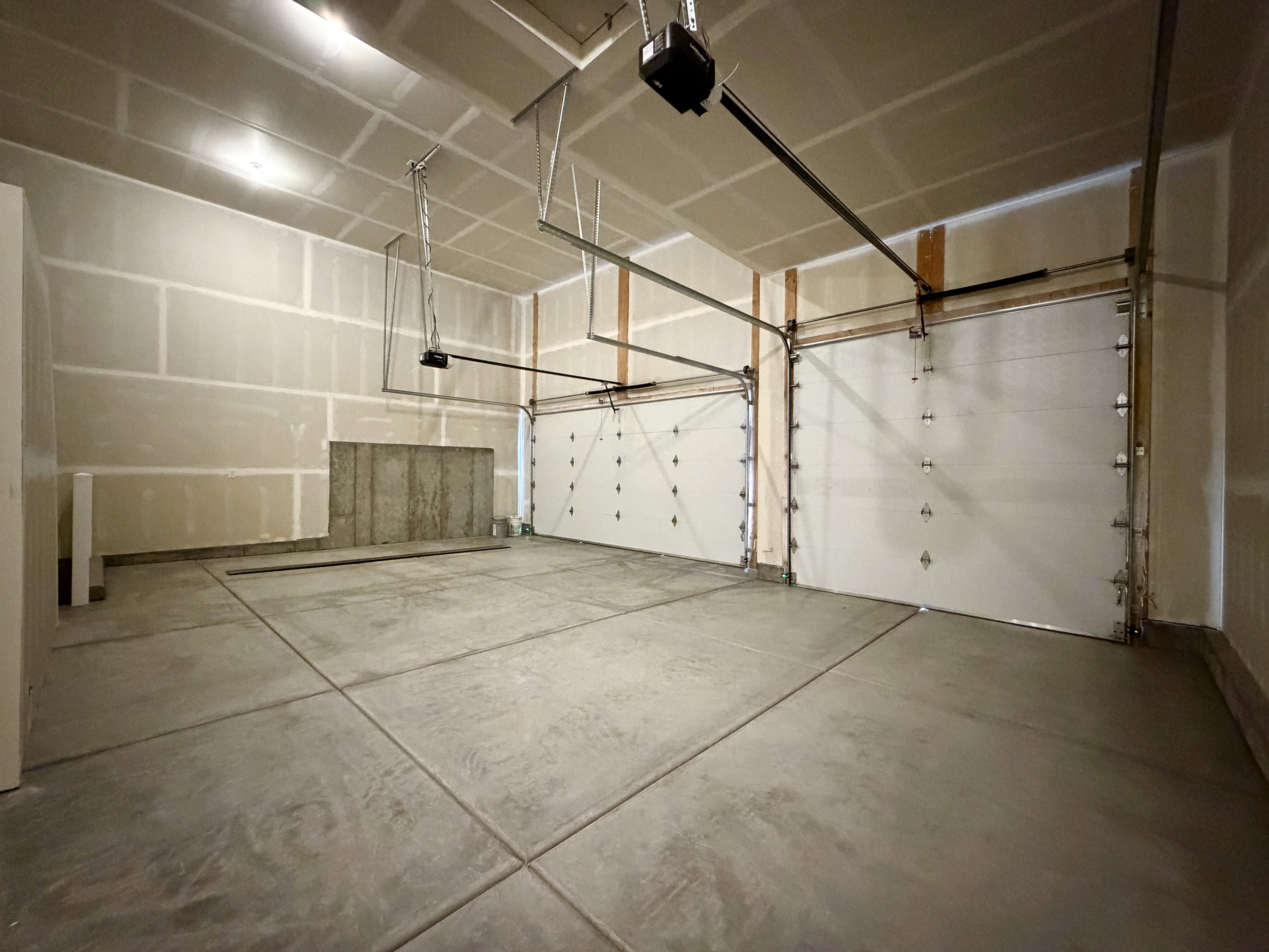 Spacious garage with exposed drywall, concrete flooring, and two overhead garage doors with openers