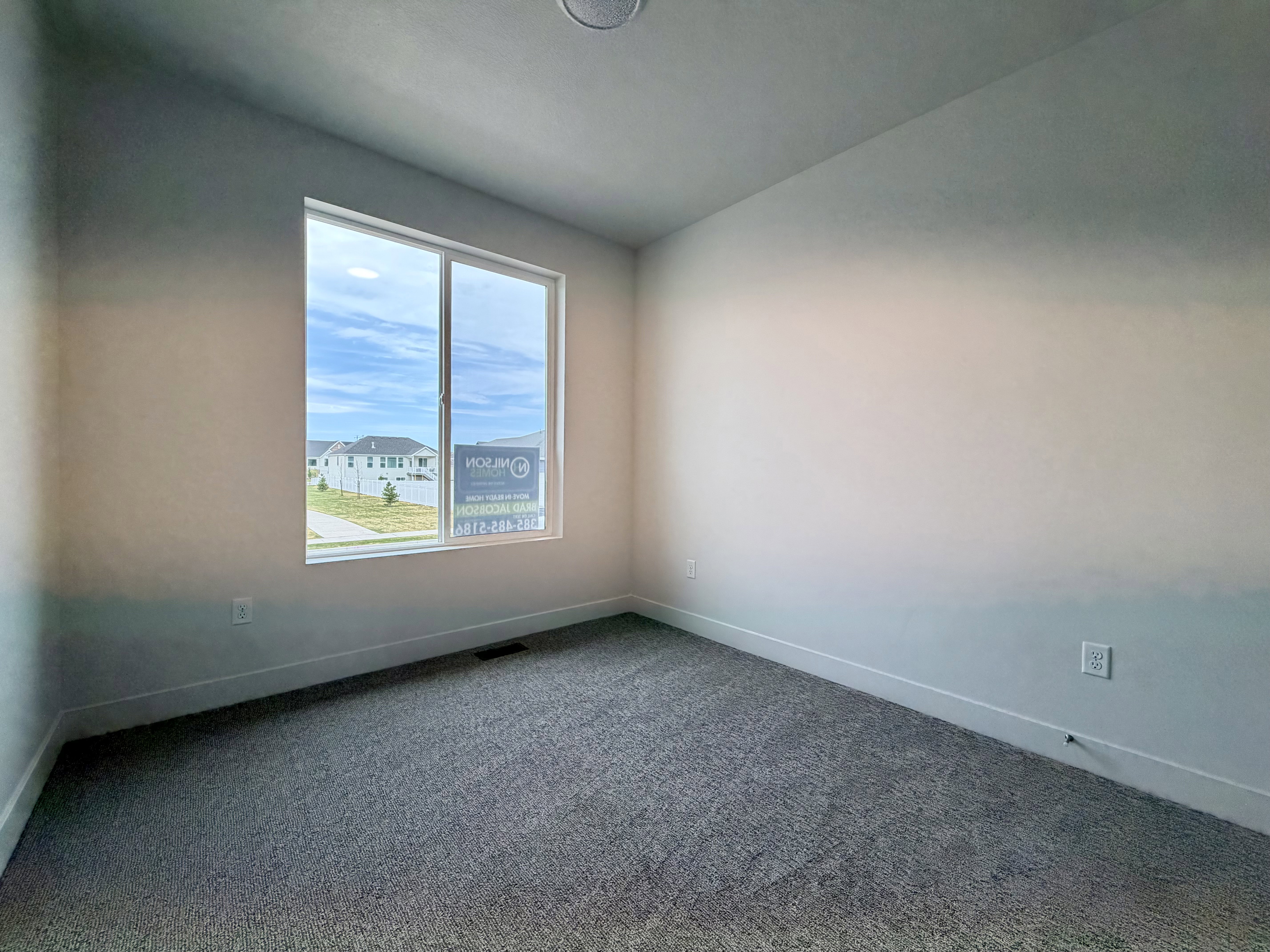 Room with a single large window, light-colored walls, and gray carpet flooring