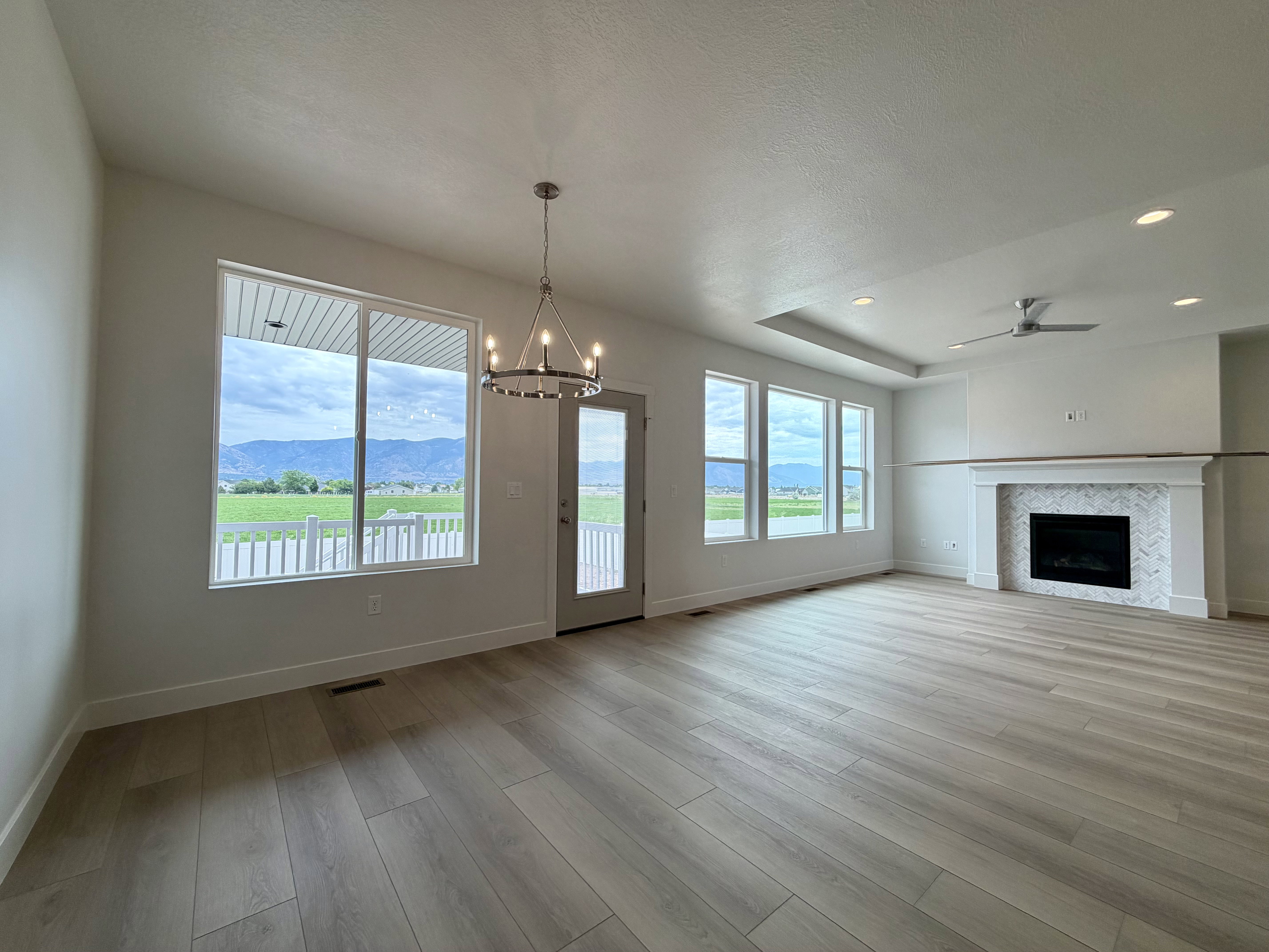Spacious living area featuring light wood-finish flooring, a contemporary fireplace with a herringbone tile surround, and large windows offering exterior scenery
