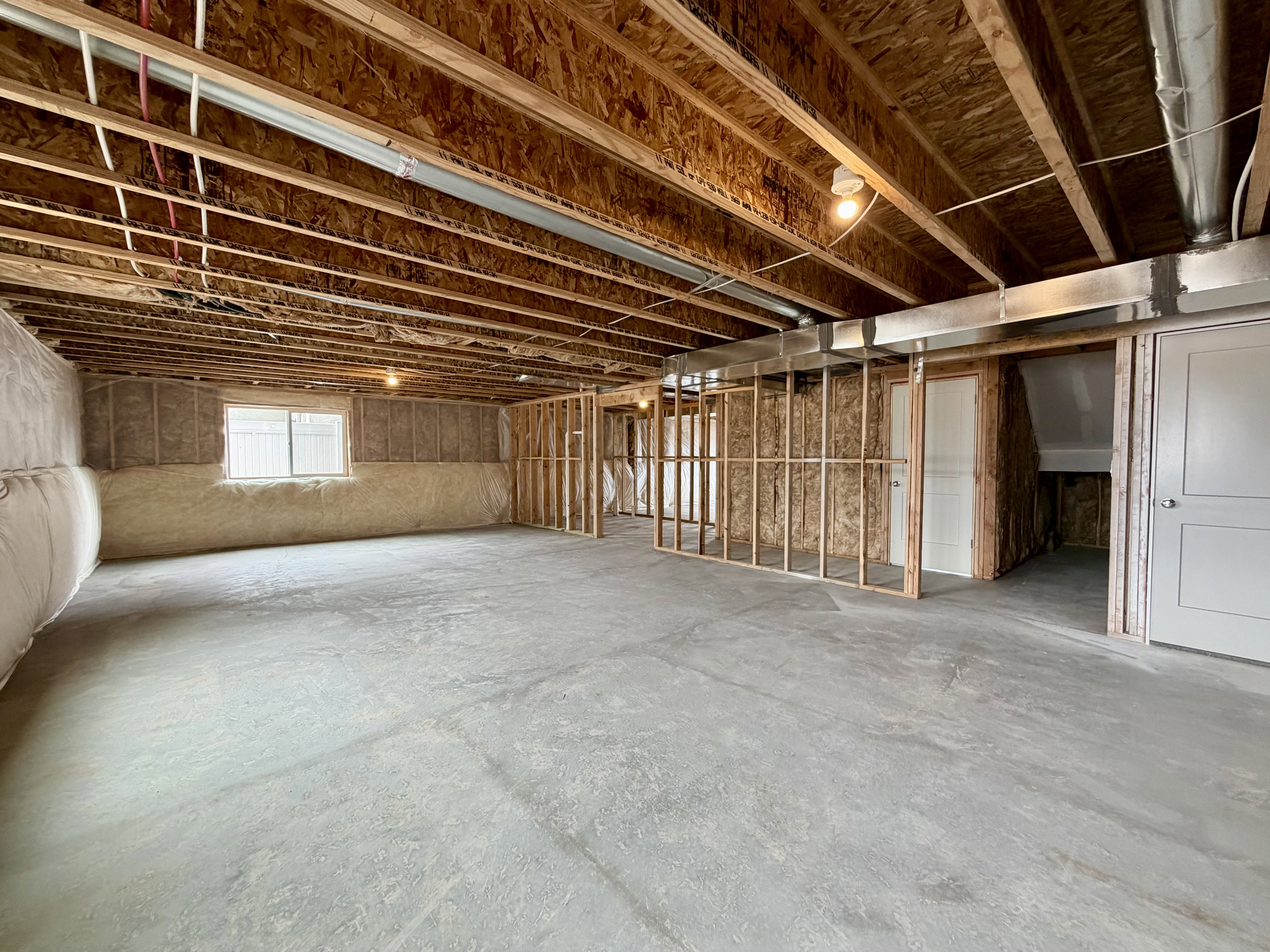 Unfinished basement featuring exposed wood joists, concrete flooring, insulated walls, framed interior walls, and a window for natural light