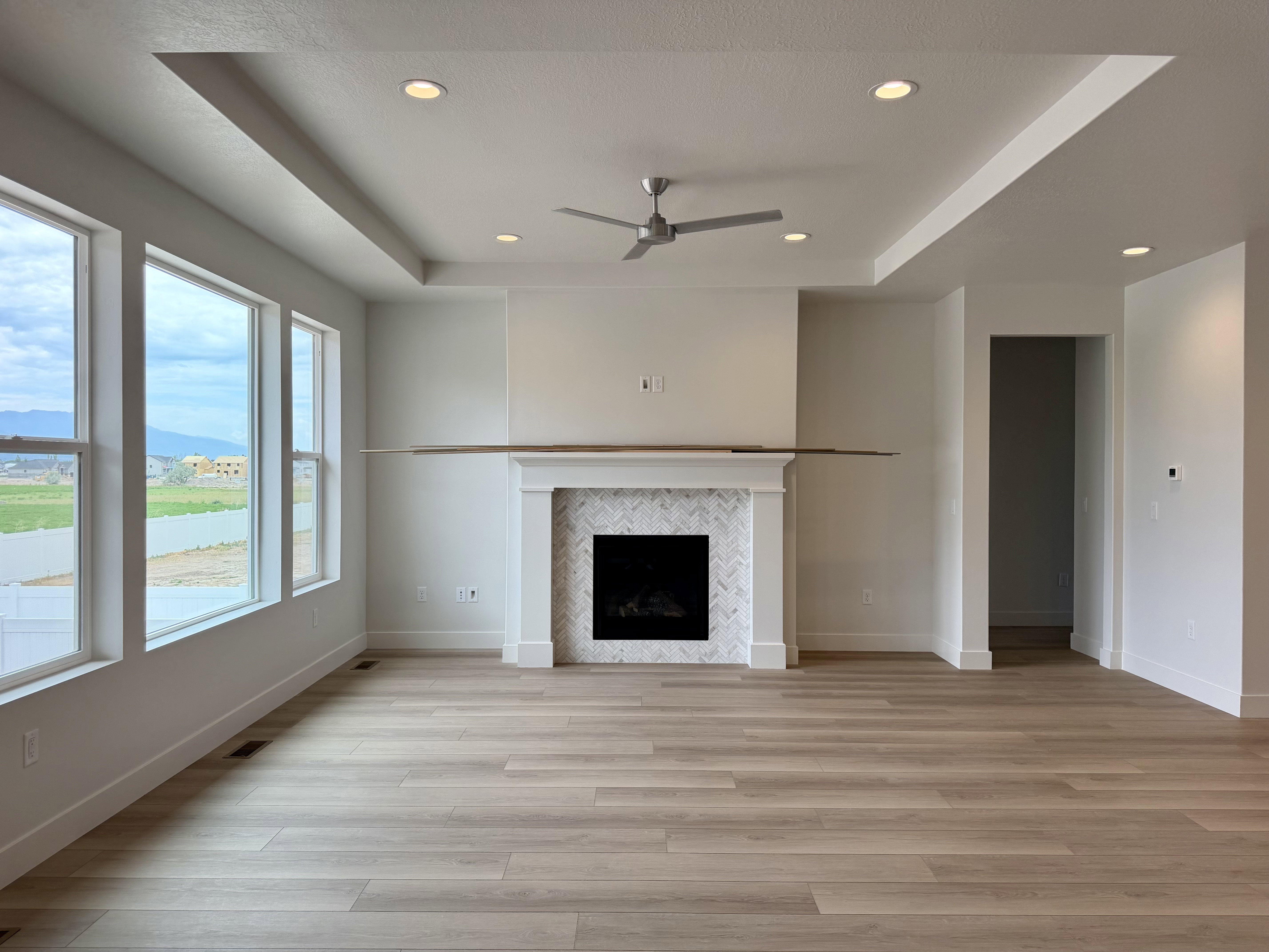 Open-concept living space featuring a fireplace with a herringbone-patterned tile surround, a mantle, and a tray ceiling with recessed lighting