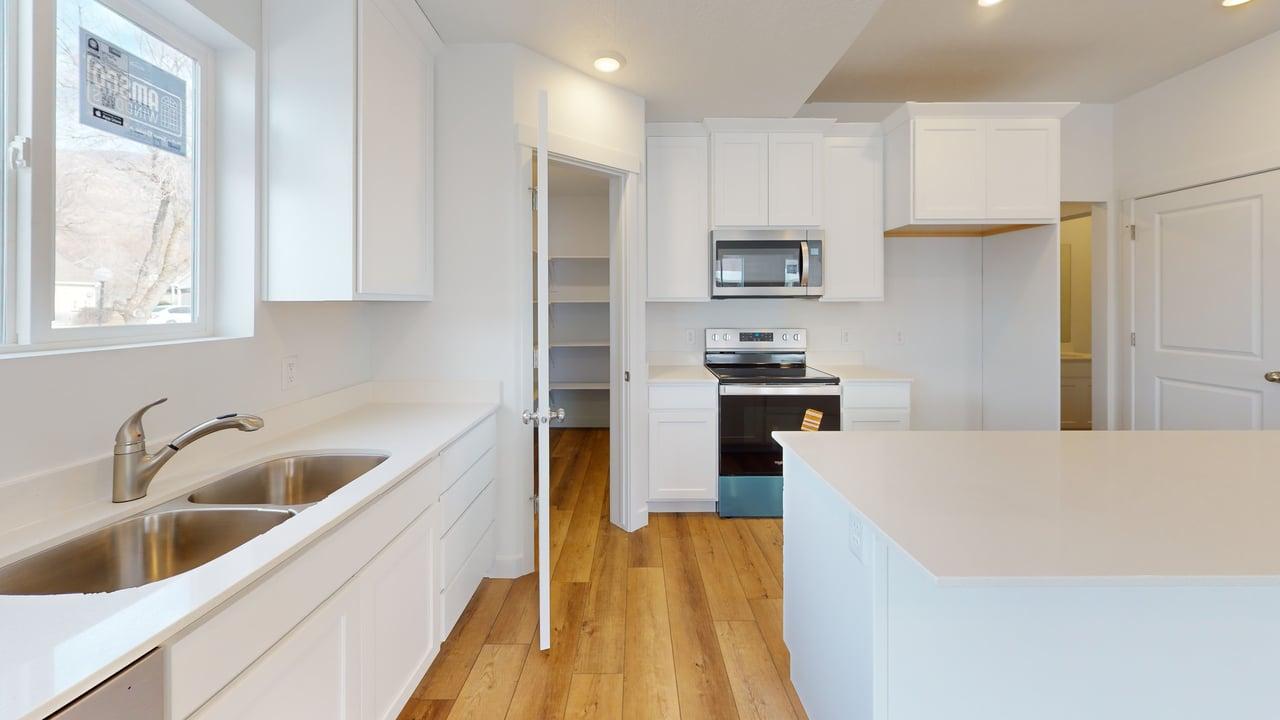 Modern kitchen featuring white cabinetry, light-toned countertops, stainless steel appliances, and wood-finish flooring