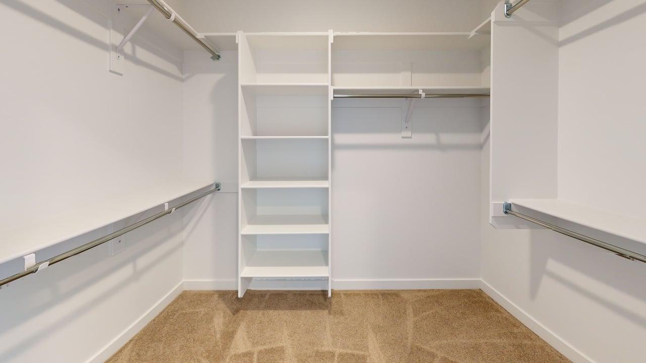 Walk-in closet featuring built-in shelving, multiple hanging rods, white walls, and carpet flooring
