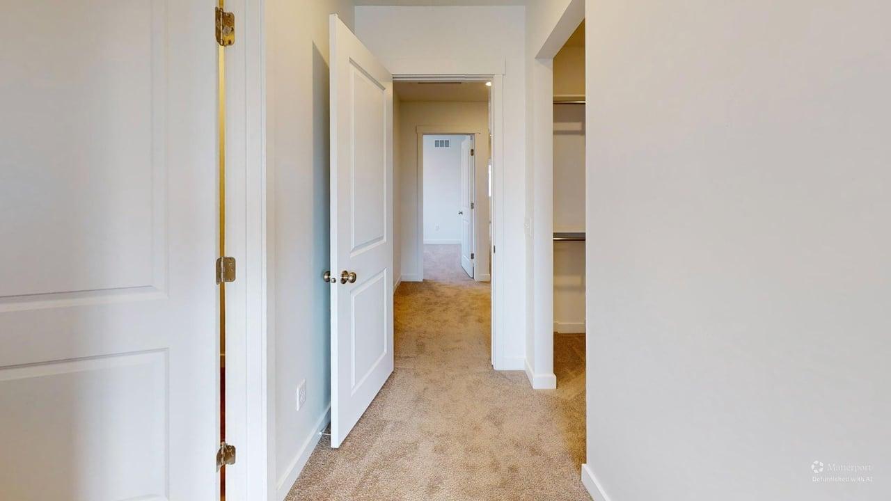 Carpeted hallway featuring white walls and white two-panel doors with brass hardware