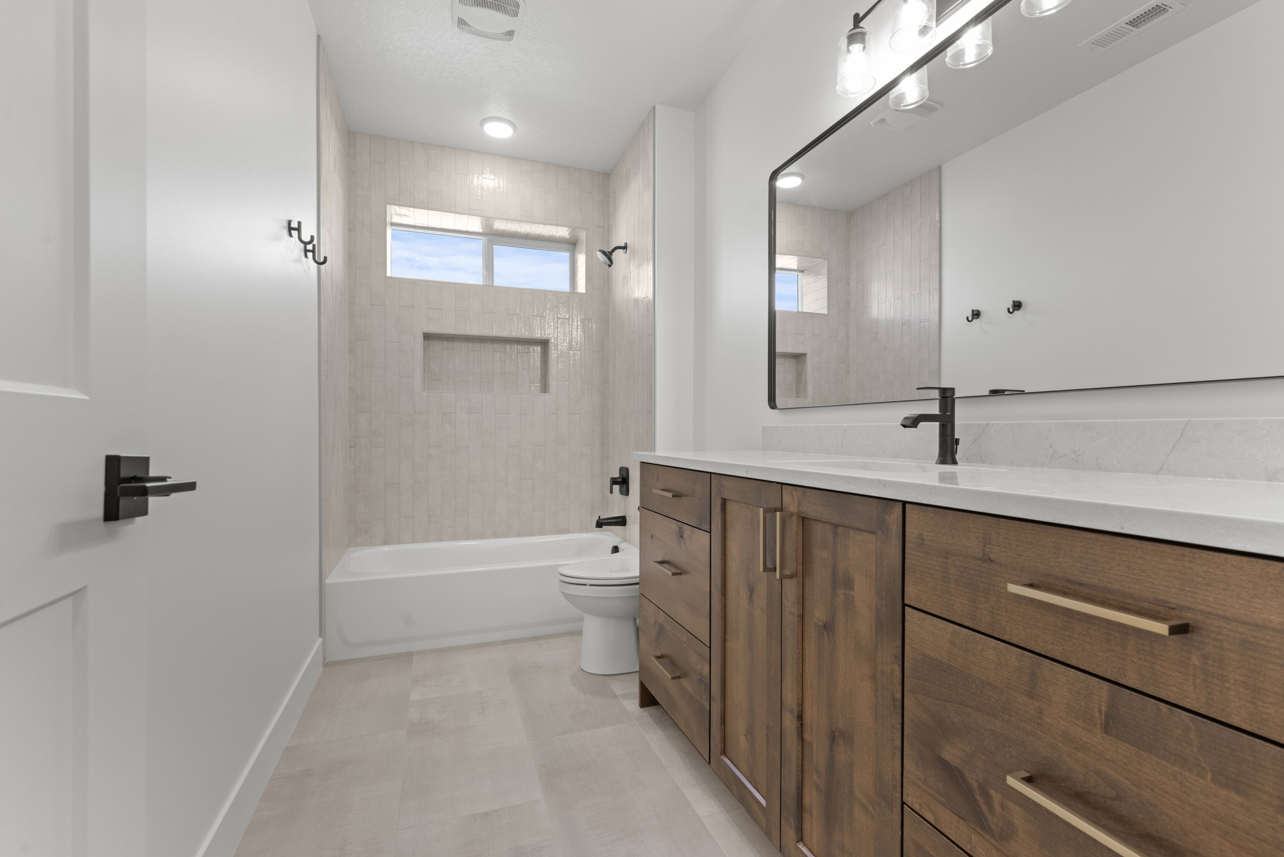 Bathroom featuring a wood-finish vanity with a light-toned countertop, a rectangular black-framed mirror, and a white bathtub with light-toned tiled walls