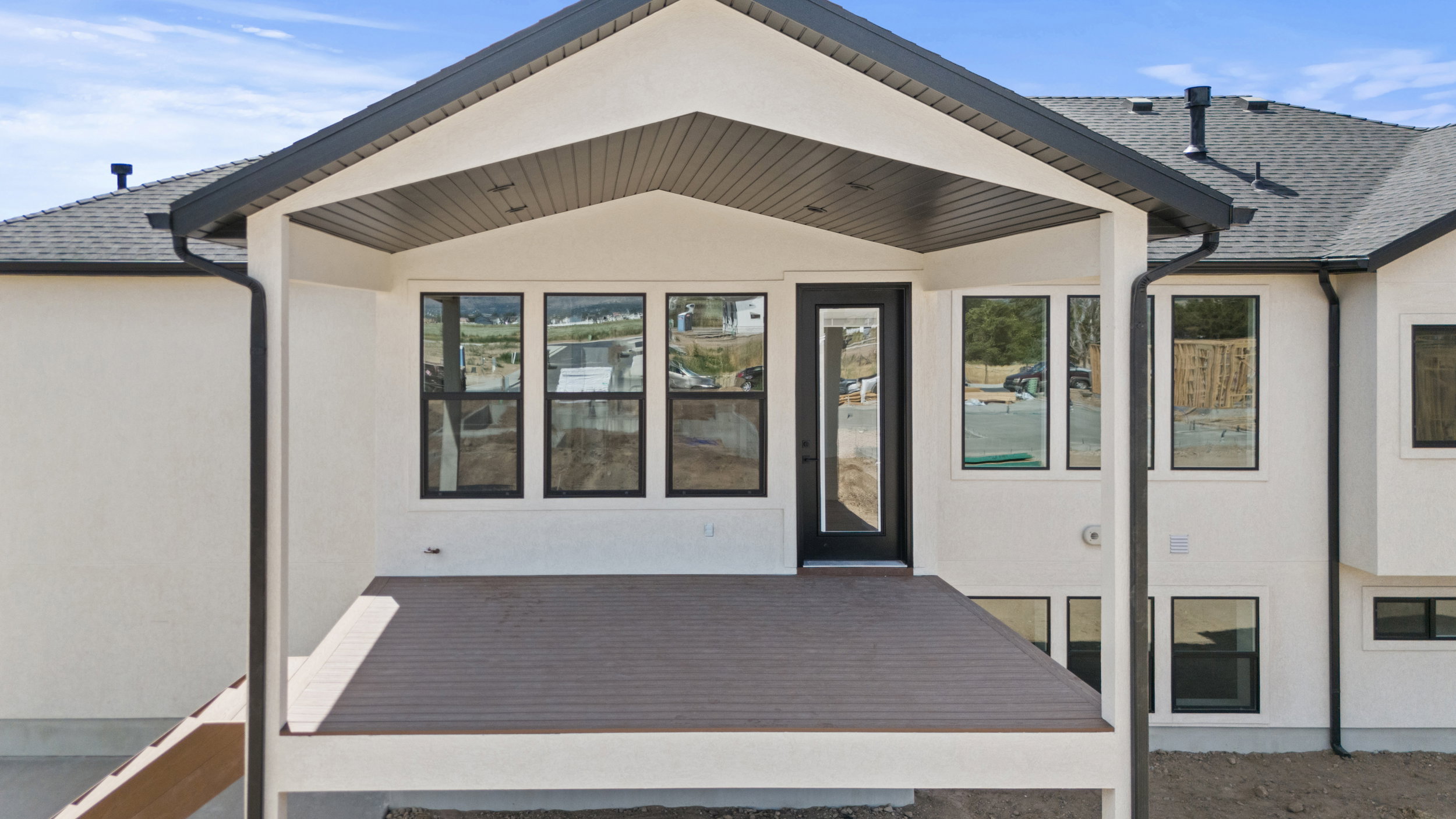 Exterior deck featuring composite decking, a covered patio area, recessed lighting, and black-framed windows and door