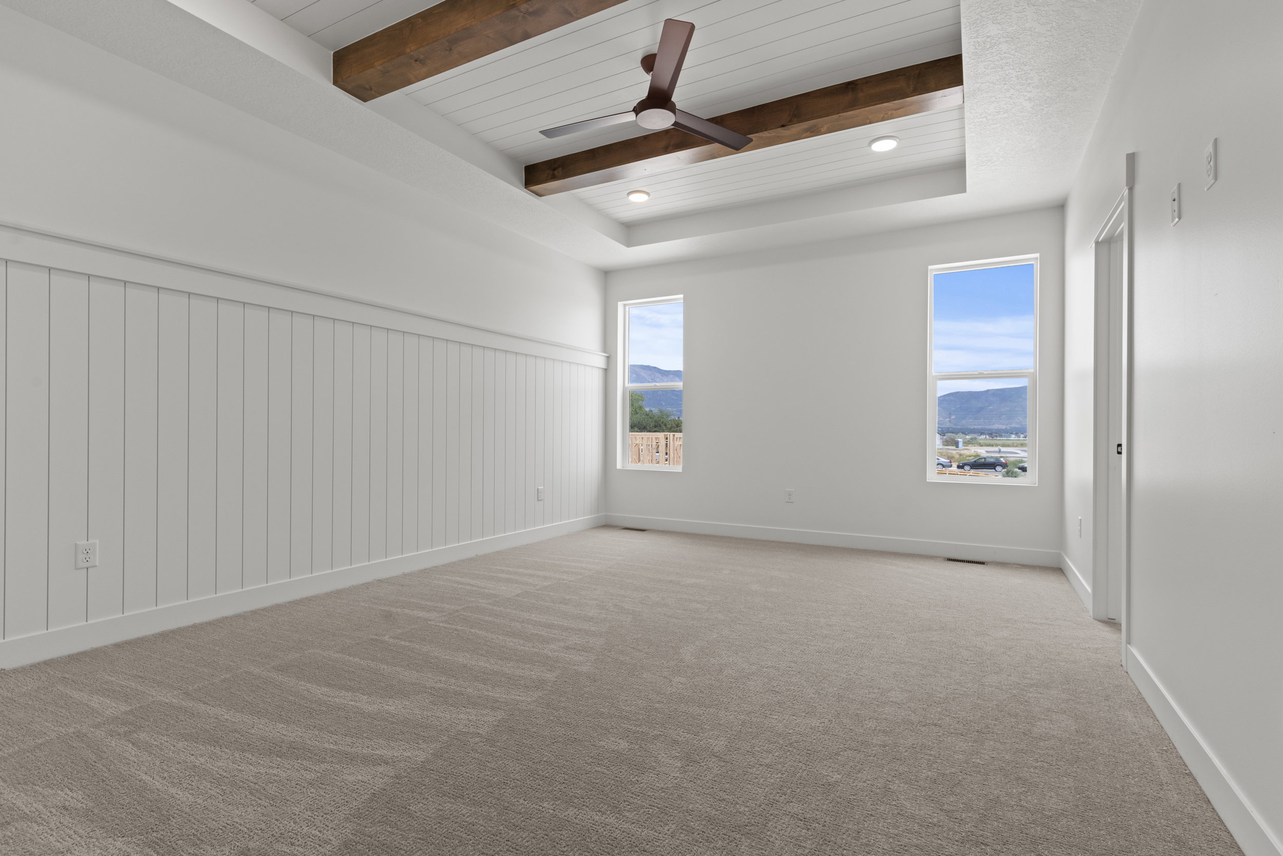Spacious room featuring a tray ceiling with wood-finish beams, integrated lighting, and a ceiling fan