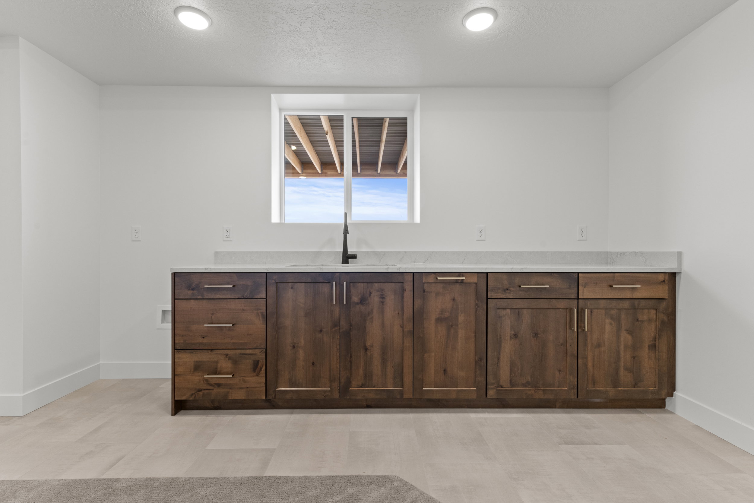 Built-in wet bar featuring dark wood cabinetry, a light-toned countertop, and a matte black faucet
