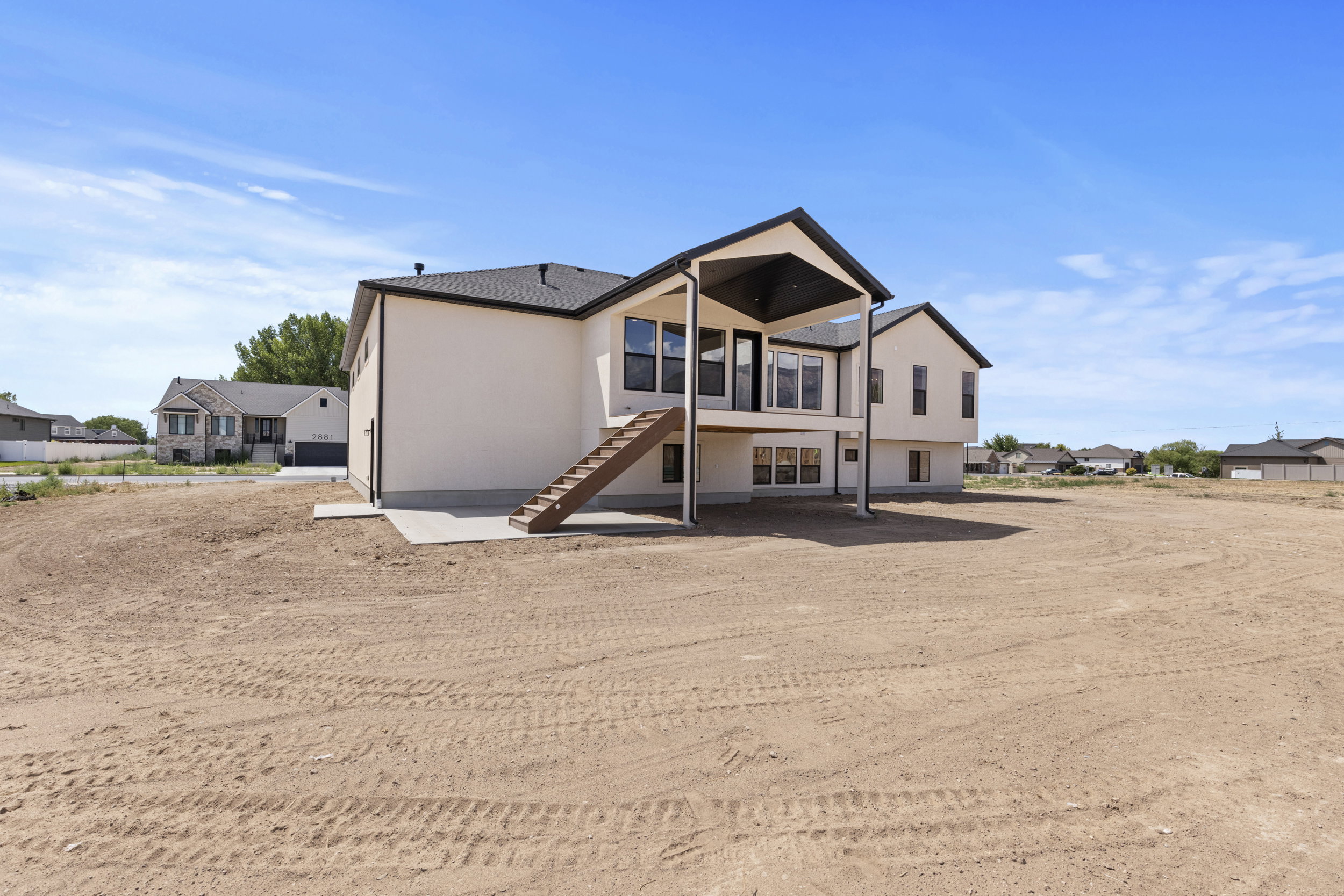 Rear exterior featuring a covered deck, lower-level patio, and a spacious, undeveloped yard