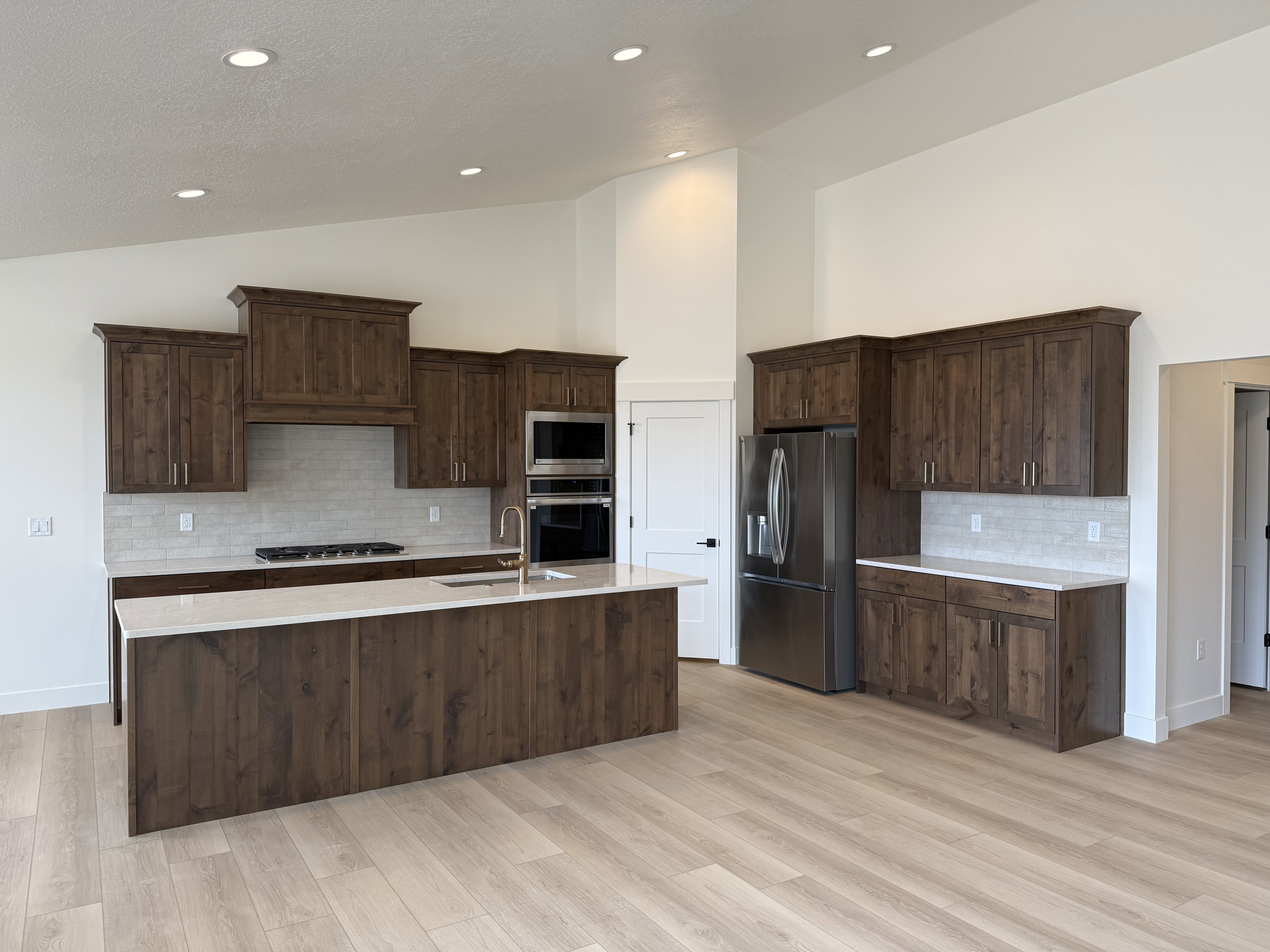 Spacious kitchen featuring rich wood cabinetry, stainless steel appliances, a large island with sink, and light-toned wood-finish flooring