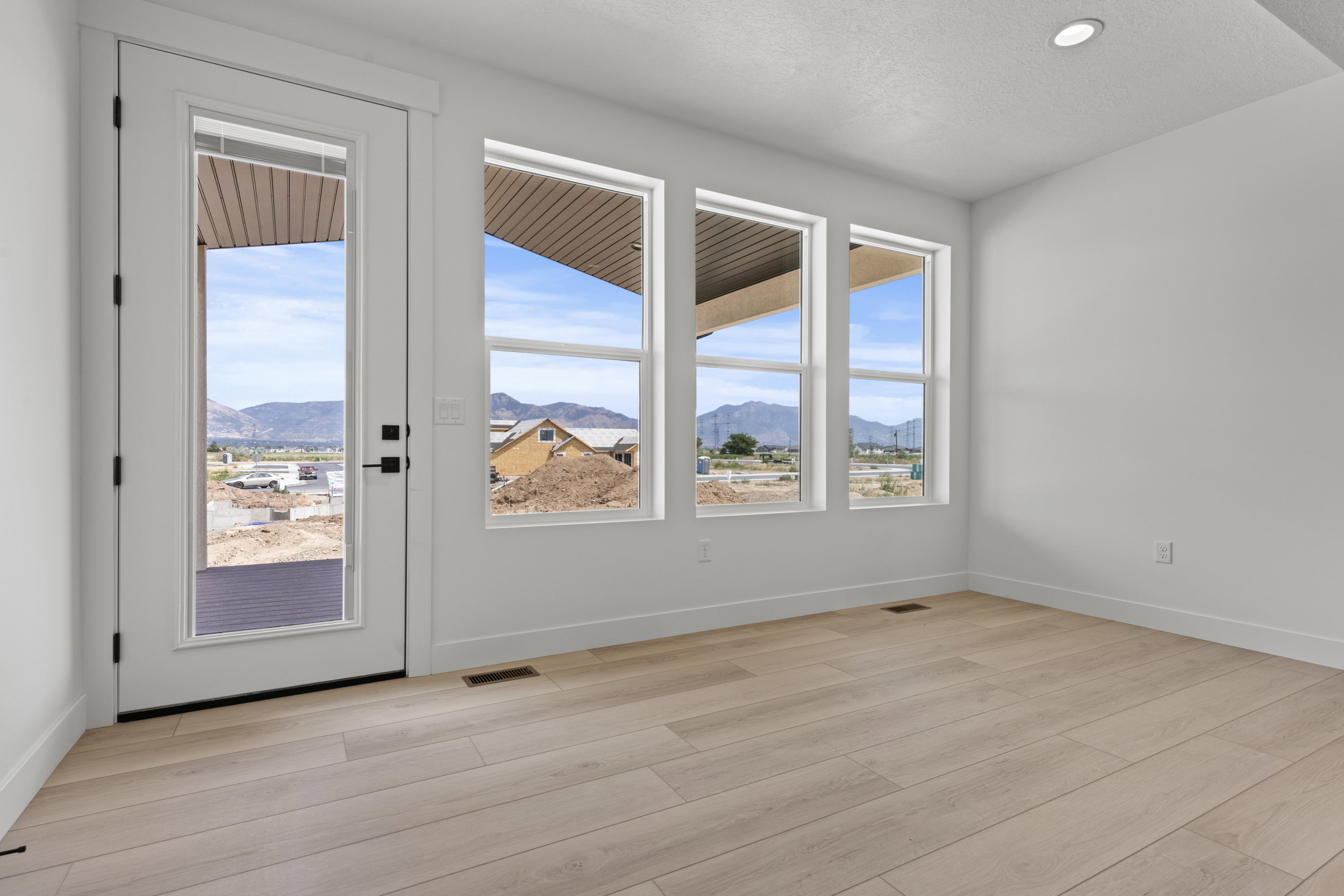 Bright interior space featuring a glass-paneled door, three expansive windows, light wood-finish flooring, and recessed ceiling lighting