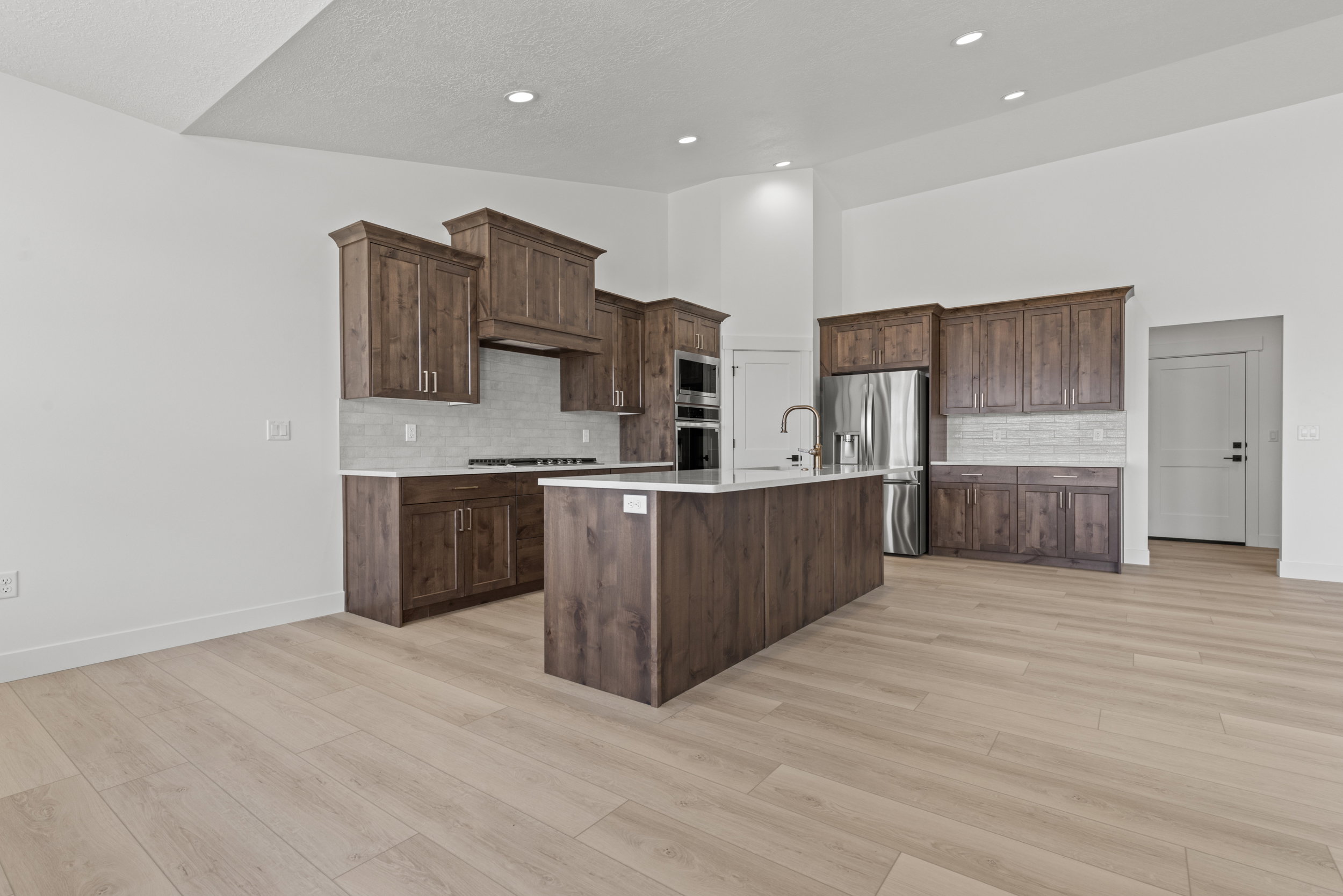 Spacious kitchen featuring dark wood cabinetry, light countertops, subway tile backsplash, a central island with sink, and recessed lighting