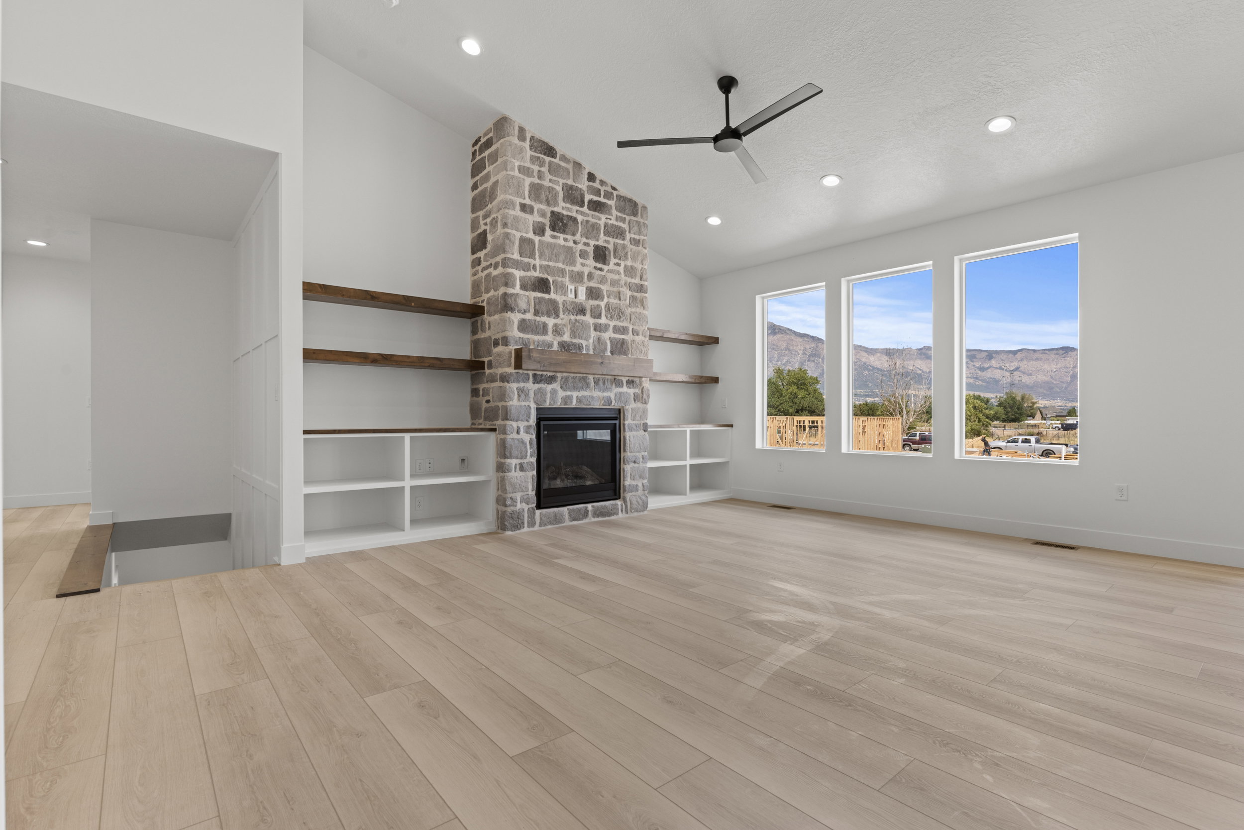 Spacious living area featuring a floor-to-ceiling stone fireplace, built-in shelving with wood-finish accents, and light wood-finish flooring
