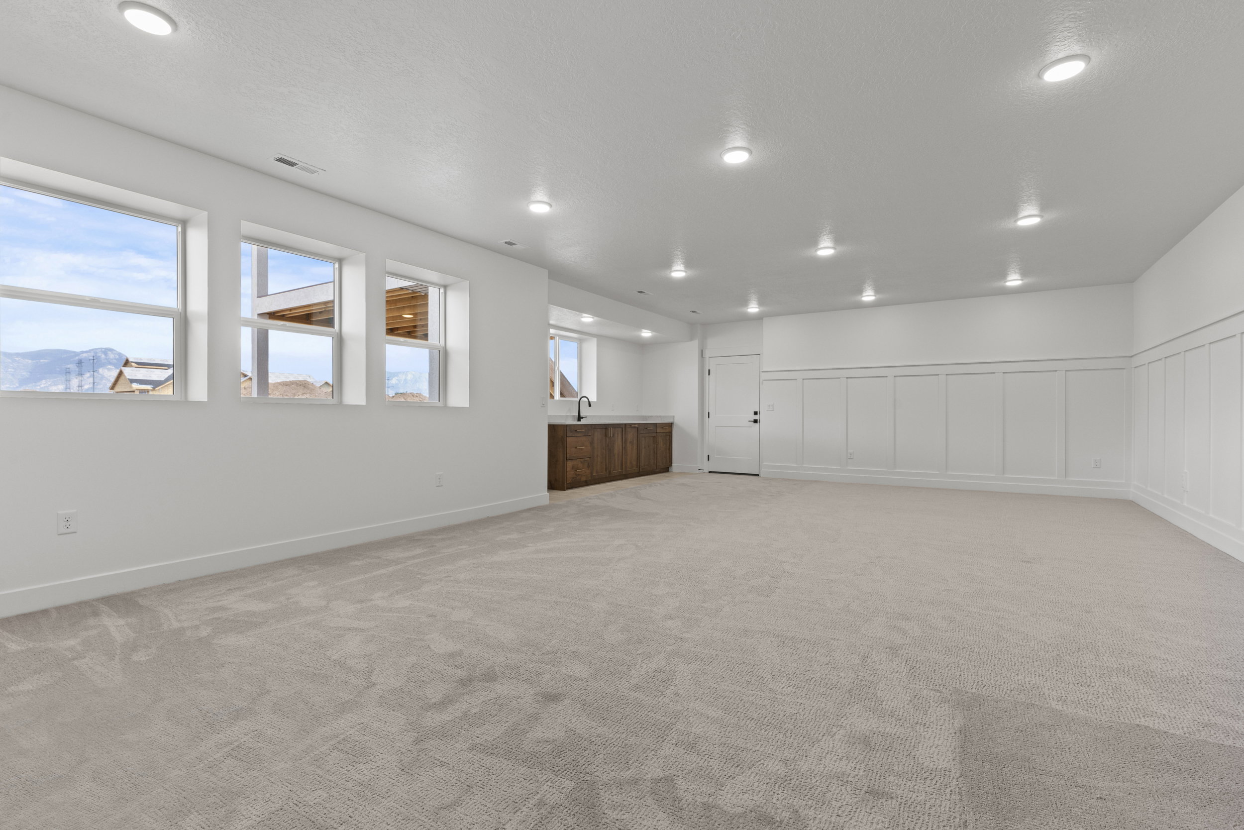 Spacious room featuring light-toned carpeting, ample recessed lighting, and a wall of three large windows