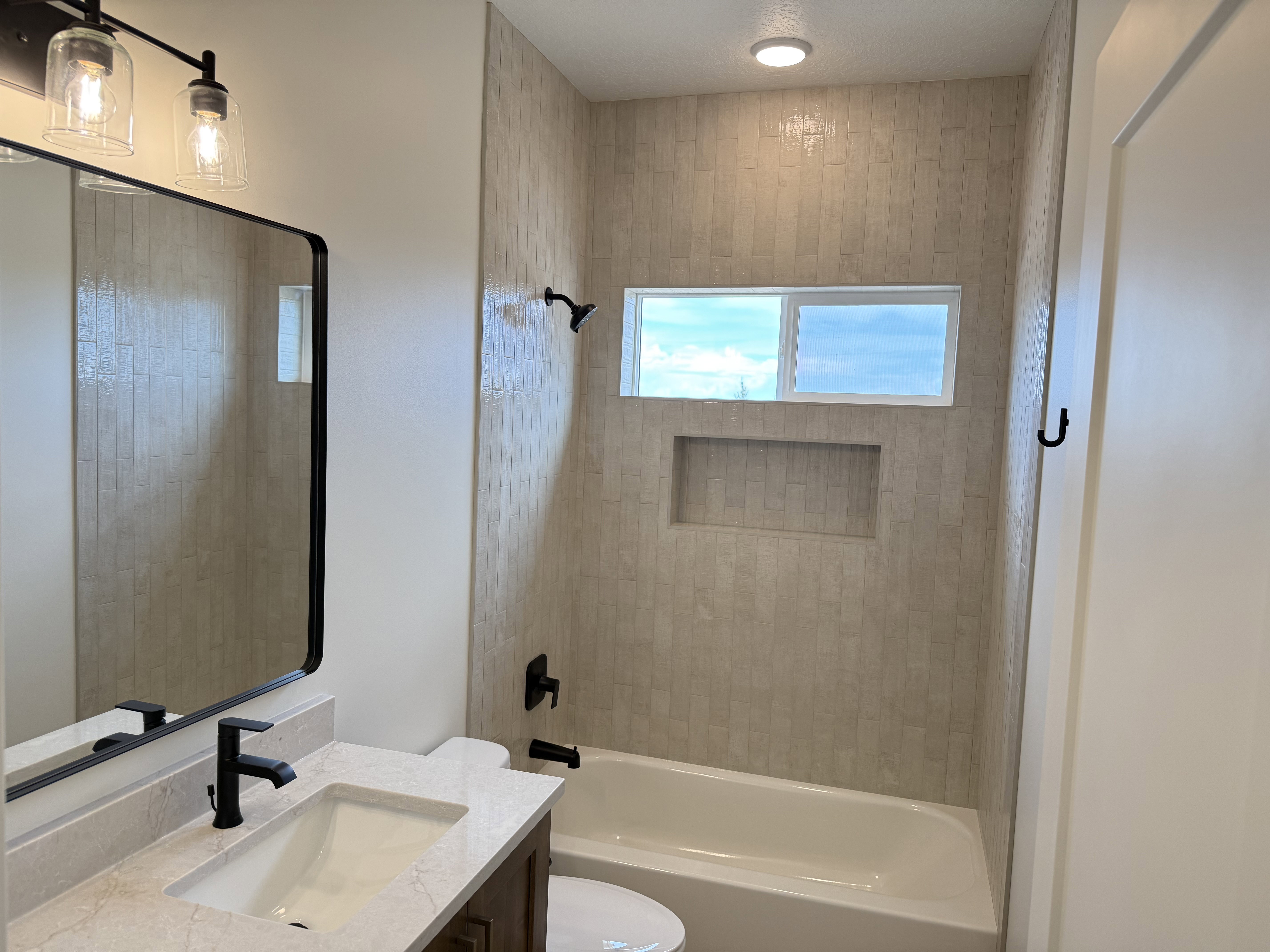 Bathroom featuring a tub/shower combination with light-toned rectangular tile surround and a recessed niche