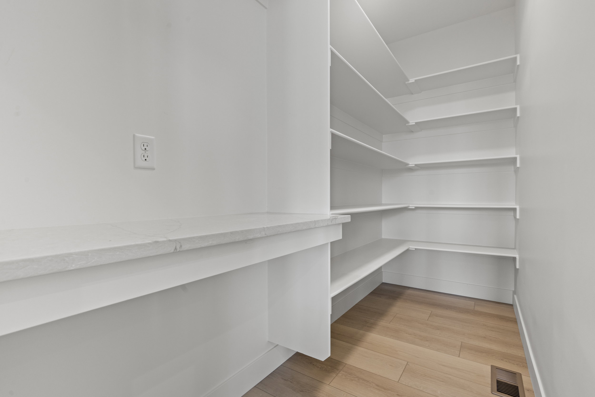 Bright white pantry with extensive built-in shelving, a dedicated counter space, and wood-finish flooring