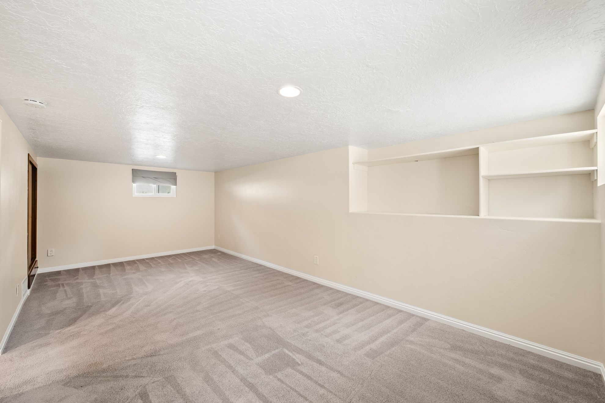 Carpeted room featuring recessed lighting, a window with a roller shade, and built-in shelving