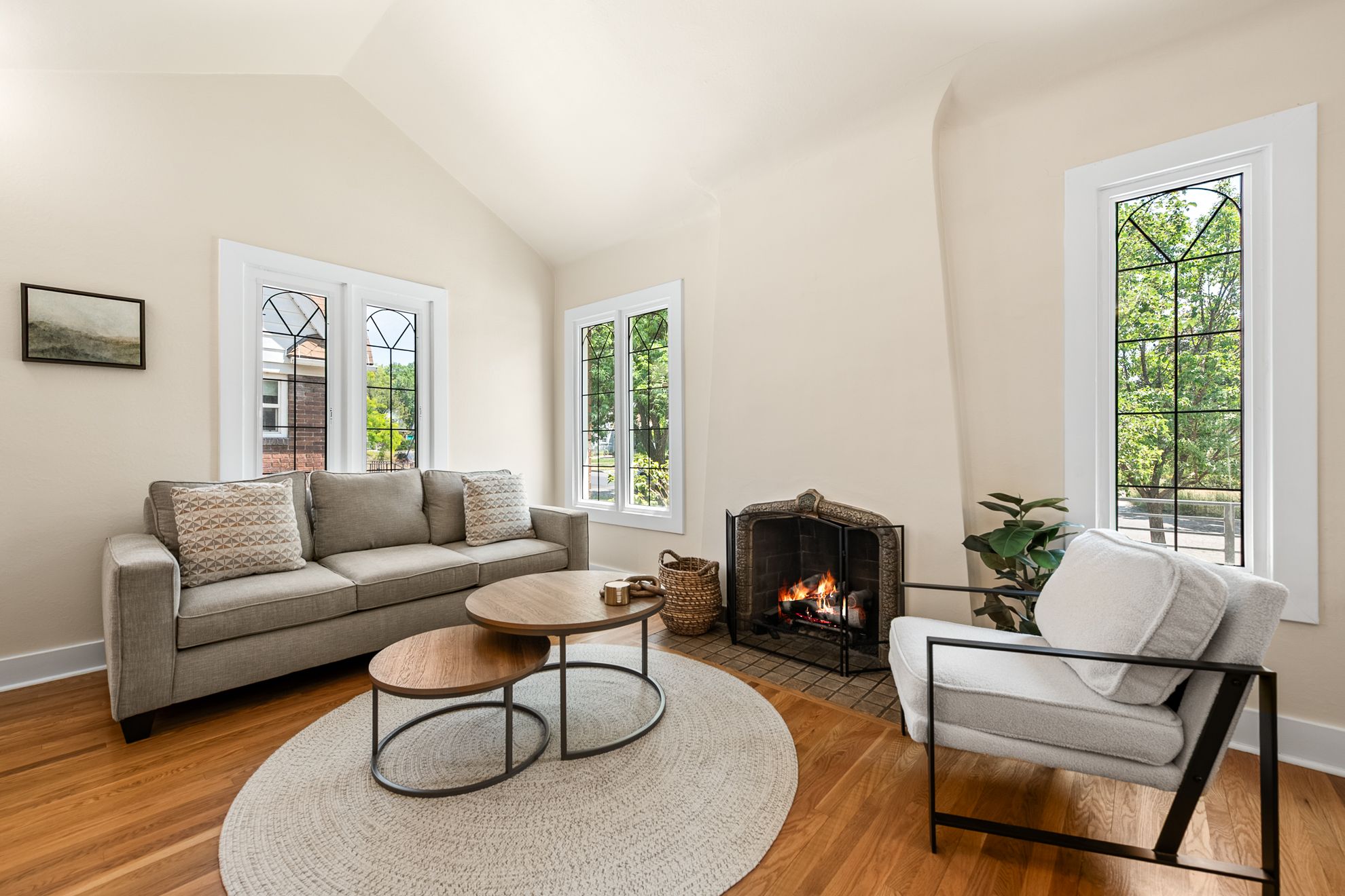 Vaulted ceiling living space with wood-finish flooring, a brick-surround fireplace, and multiple leaded-glass windows