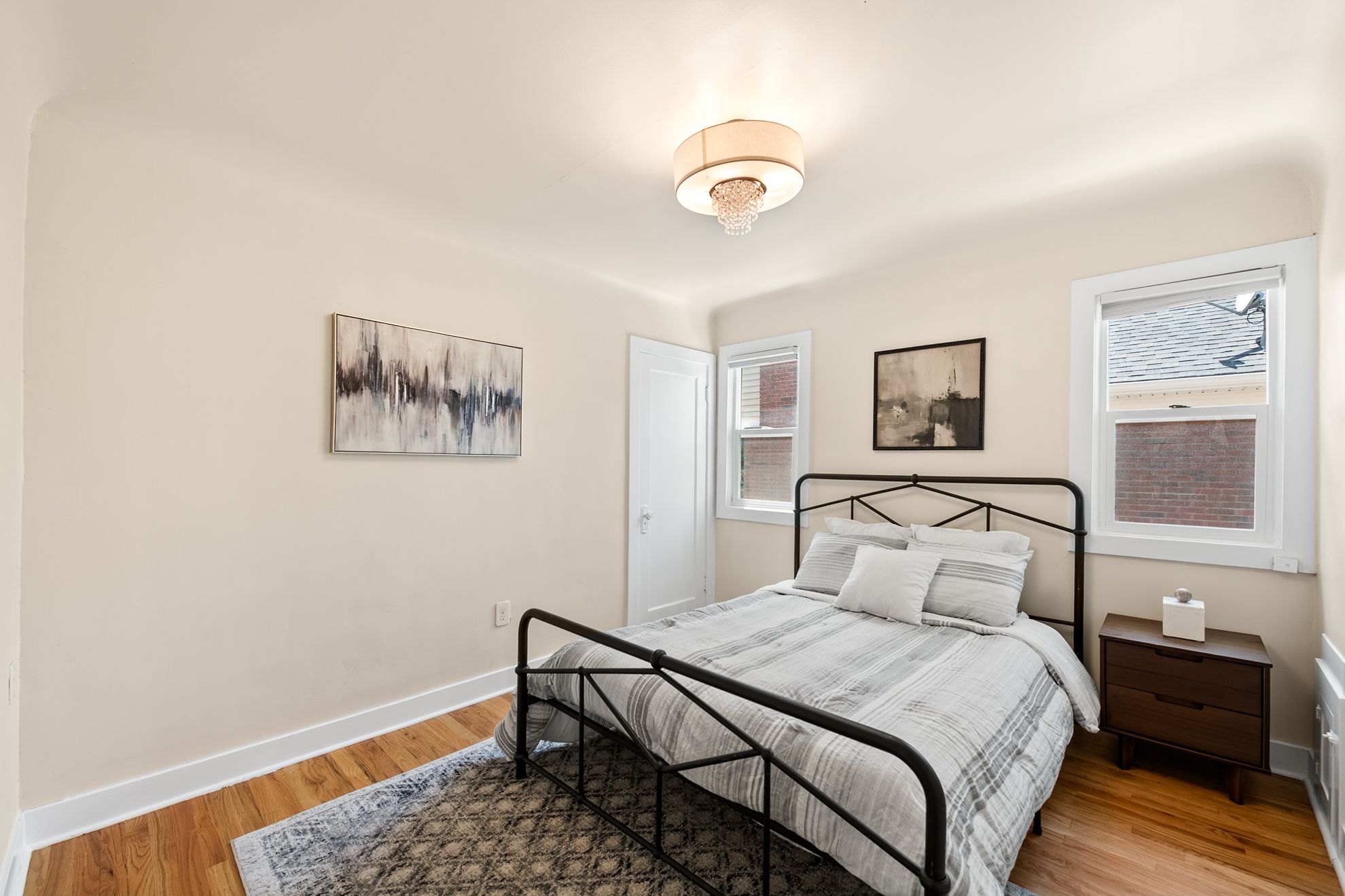 Bedroom featuring two windows, wood-finish flooring, a white paneled door, and a semi-flush mount ceiling fixture with a drum shade