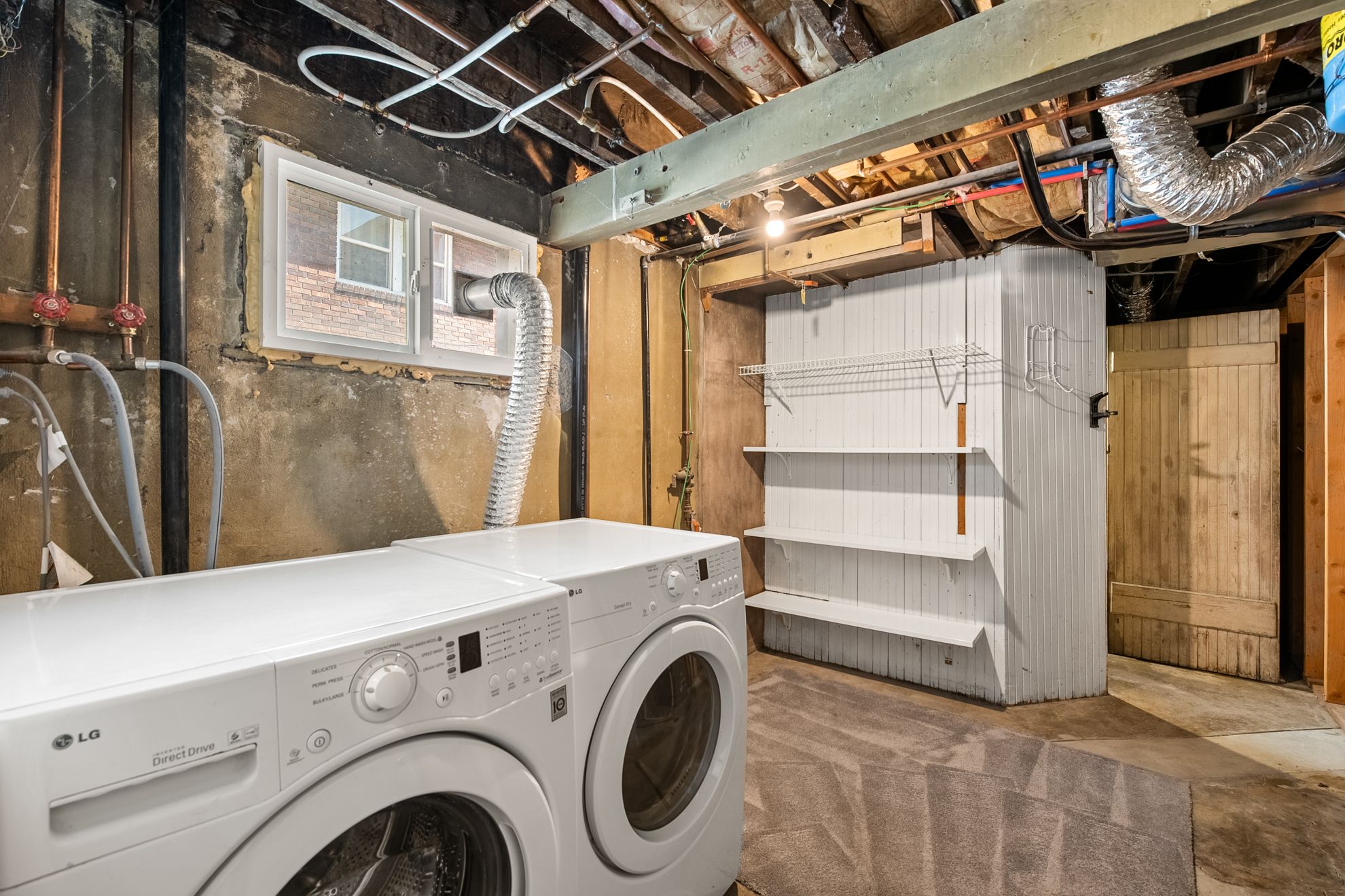 Basement laundry area featuring a utility window, exposed ceiling joists, and a built-in storage unit with shelving