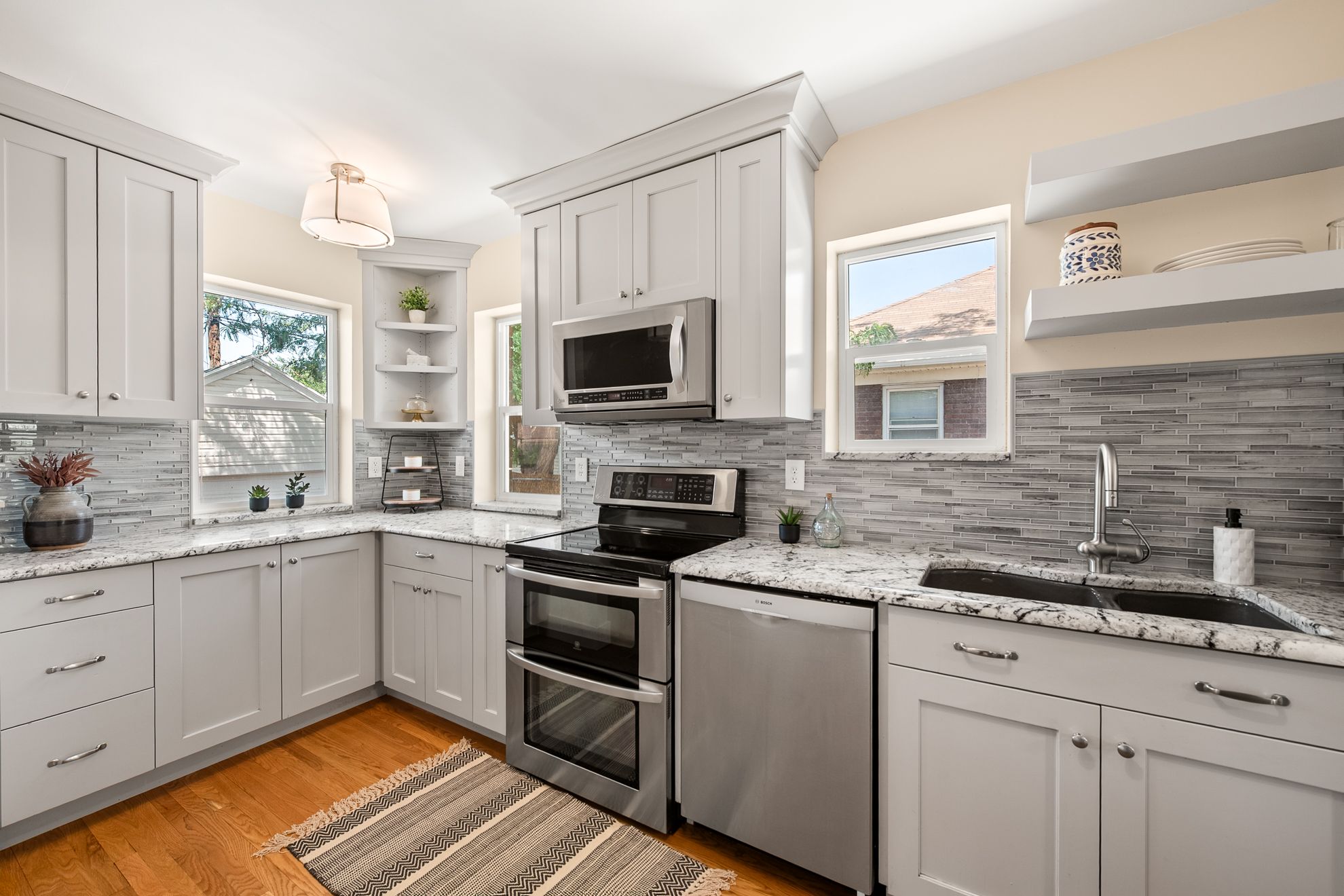 Kitchen featuring light gray shaker cabinetry, wood-finish flooring, stainless steel appliances, white patterned countertops, and a gray subway tile backsplash