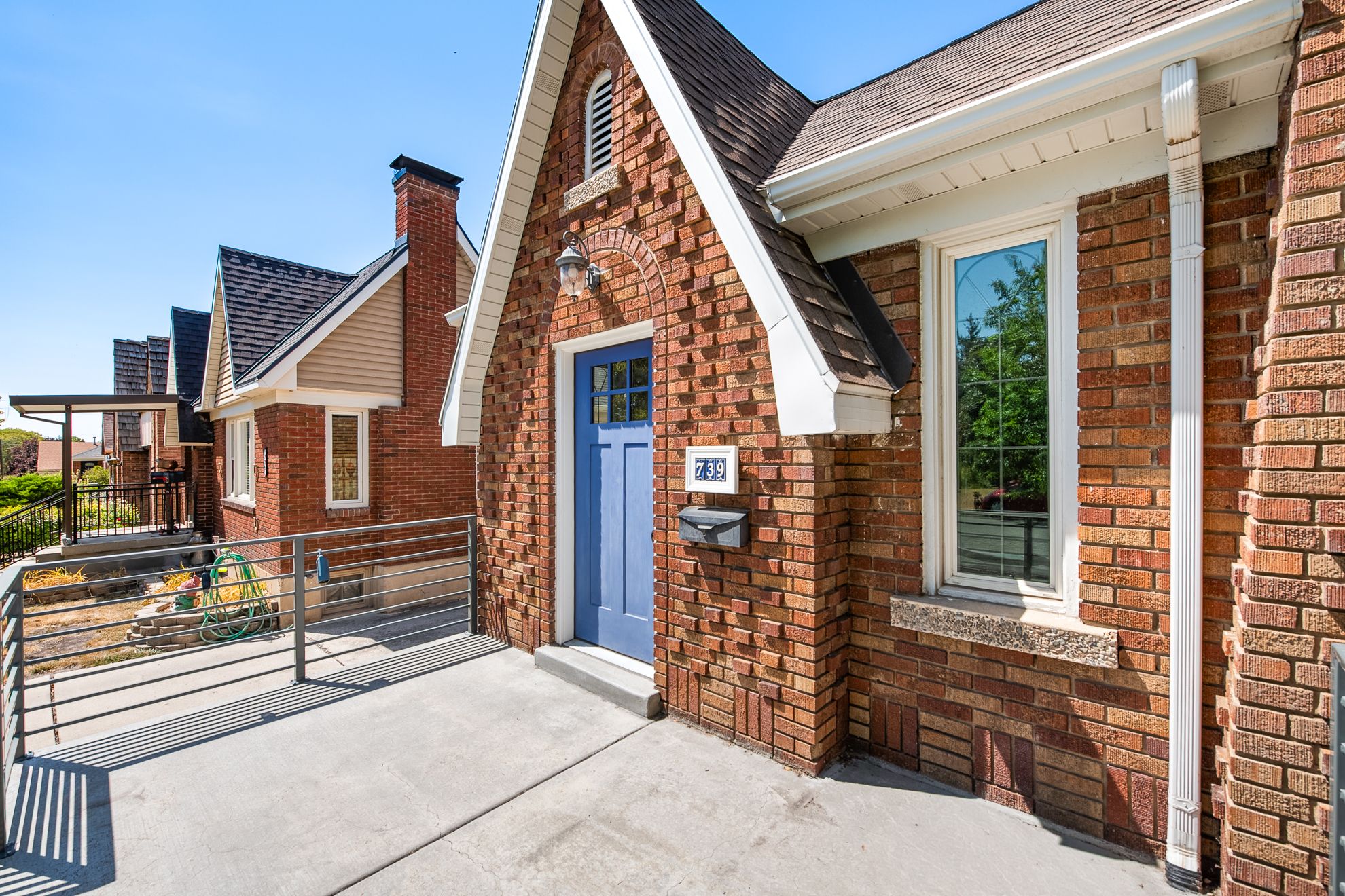 Brick exterior featuring a gabled roofline, a blue entry door with transom window, and a concrete patio with horizontal railings
