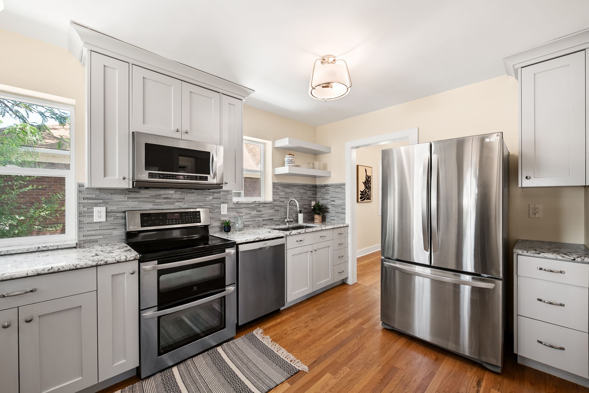 Kitchen featuring stainless steel appliances, light gray shaker cabinetry, speckled countertops, and a gray subway tile backsplash