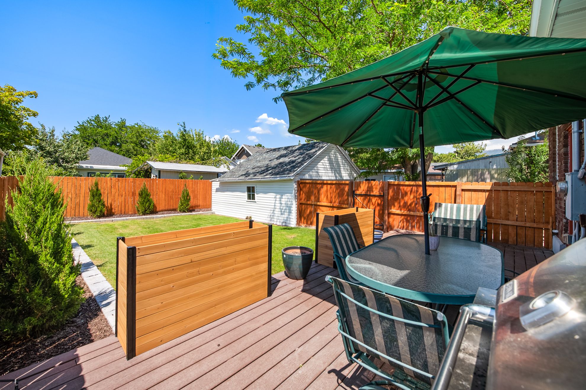Expansive backyard featuring a wood-composite deck, manicured lawn, and mature trees