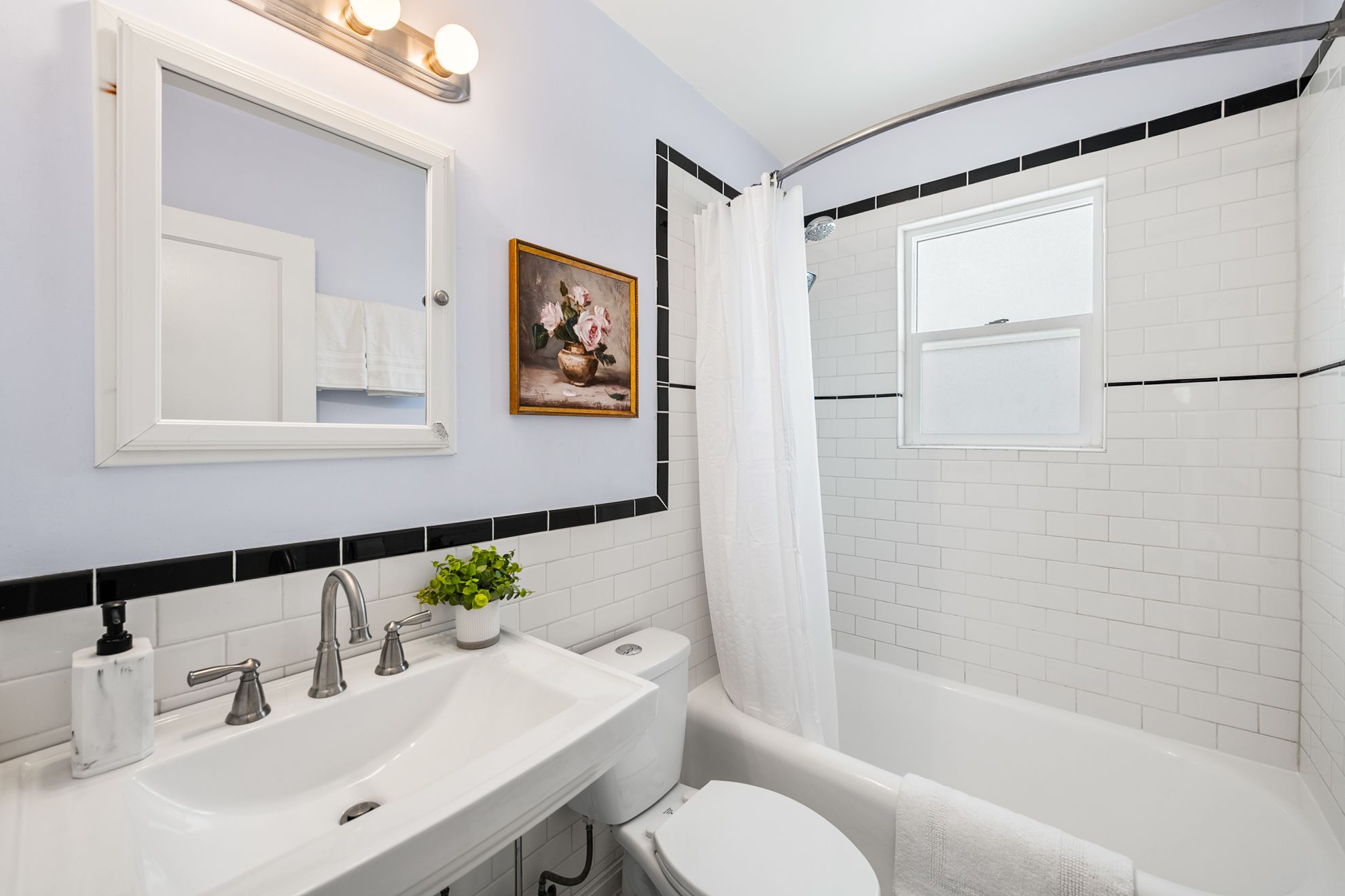 Bathroom featuring a pedestal sink with dual-handle faucet, a framed mirror, and a wall-mounted light fixture