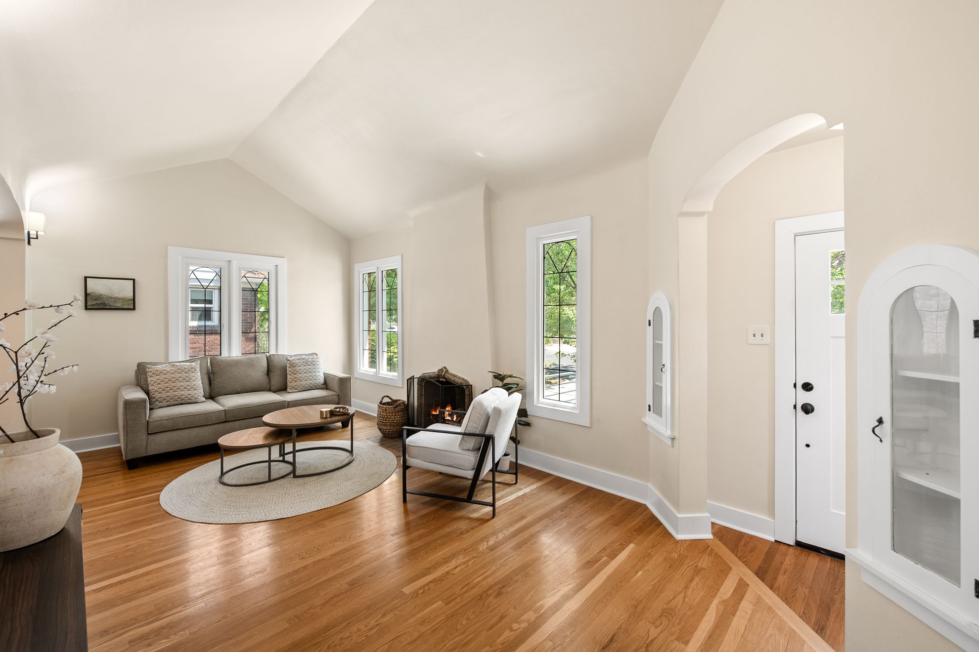 Spacious living area featuring vaulted ceilings, wood-finish flooring, multiple windows providing ambient light, an arched doorway, and built-in display cabinetry
