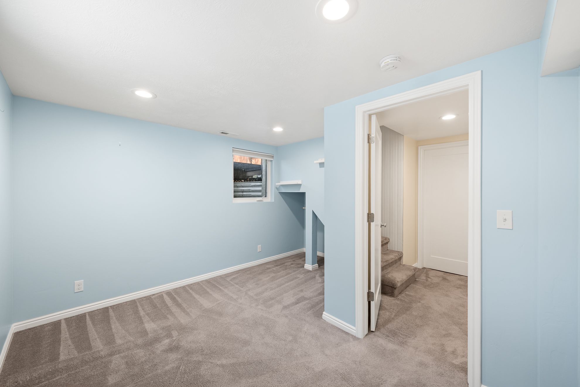 Spacious room featuring light blue walls, gray carpet, white baseboards, and recessed lighting