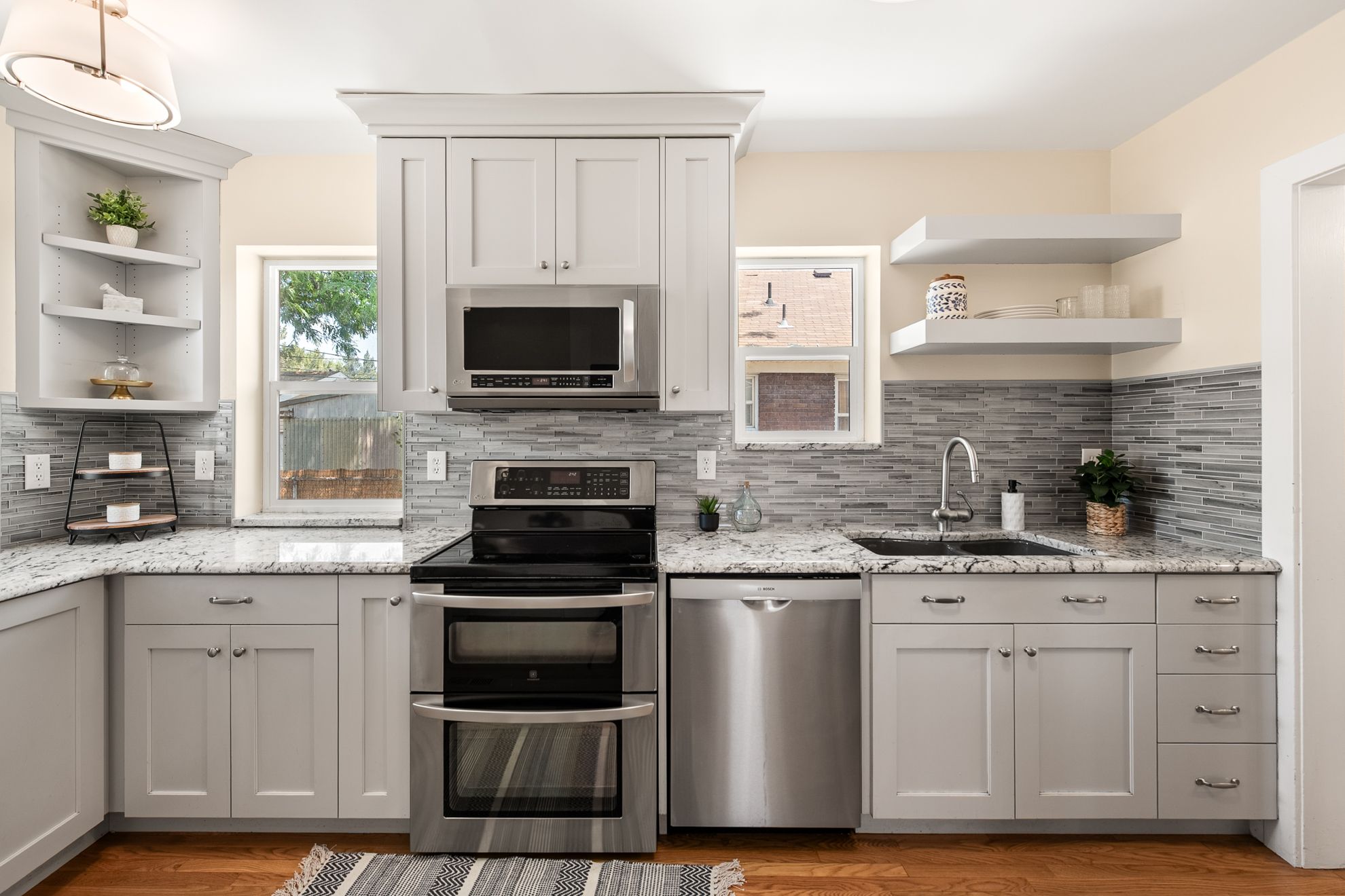 Contemporary kitchen featuring light gray cabinetry, stainless steel appliances, granite countertops, and a mosaic tile backsplash