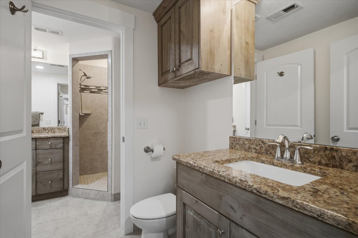 Bathroom featuring a shower enclosure with tiled walls, dual vanities with stone countertops, and wood-finish cabinetry