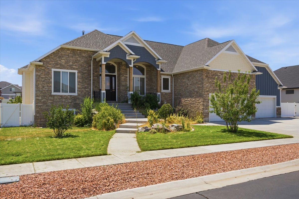 Contemporary craftsman-style exterior featuring a stone and siding facade, covered entry porch with columns, a multi-car garage, and a manicured lawn with mature landscaping