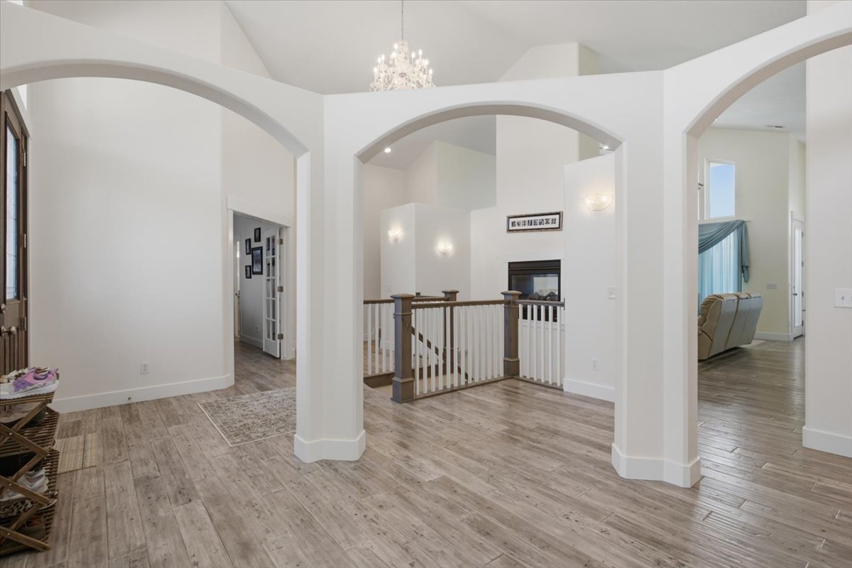 Open-concept entryway featuring wood-finish flooring, multiple arched doorways, a prominent staircase with a wood and white railing, a built-in fireplace, and vaulted ceilings