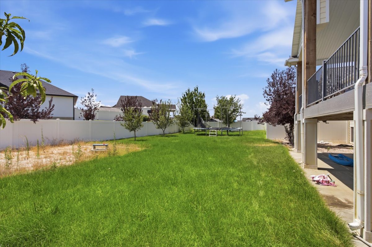 Spacious backyard with a large lawn area, mature trees, privacy fencing, and an upper-level deck with metal railings
