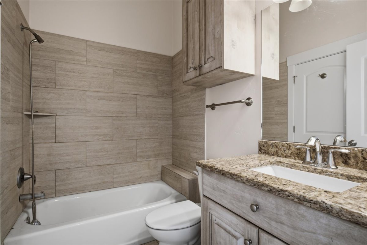 Bathroom featuring a white bathtub, tiled shower surround, a vanity with a stone-finish countertop, and a wall-mounted mirror