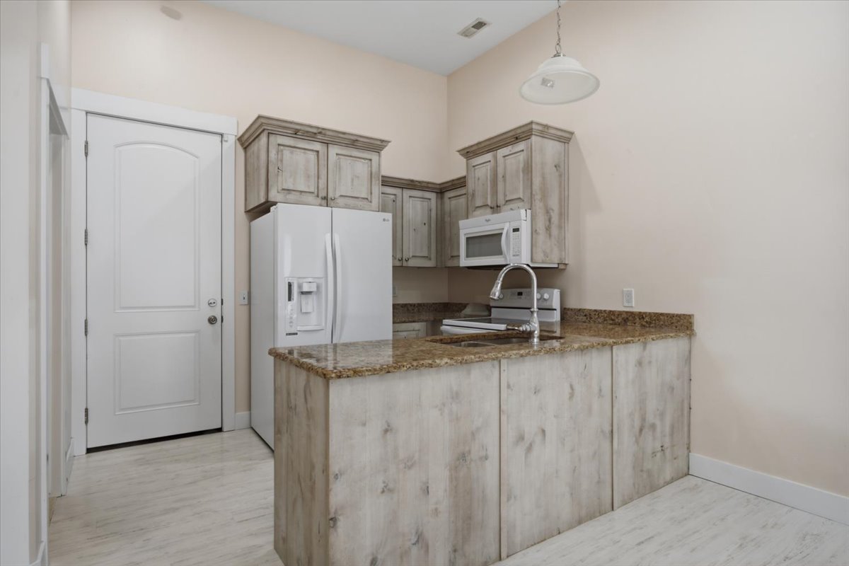Compact kitchen area featuring distressed wood-finish cabinetry, a granite-style countertop, and a stainless steel sink with a gooseneck faucet