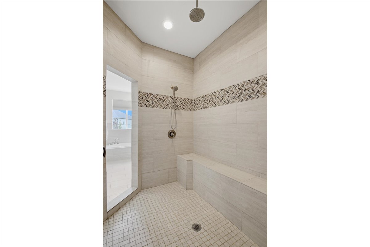 Spacious shower featuring light-toned large format wall tiles, a mosaic accent band, a built-in bench, a rain showerhead, and a handheld shower fixture
