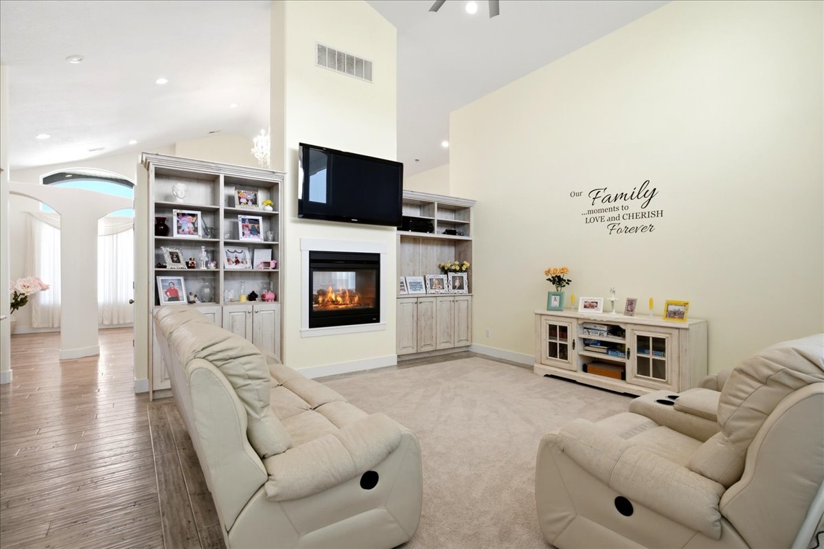 Living area featuring a floor-to-ceiling fireplace, integrated shelving, vaulted ceilings, recessed lighting, and wood-finish flooring