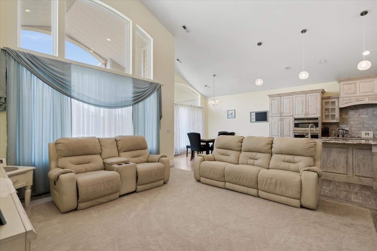 Open-concept living space featuring vaulted ceilings, a kitchen with distressed cabinetry and stone backsplash, recessed lighting, and large picture windows