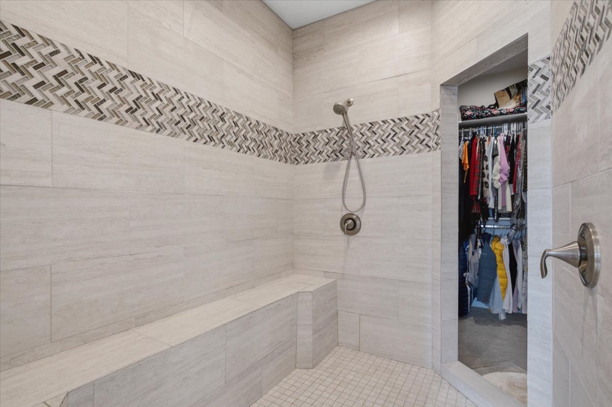 Spacious walk-in shower featuring large format tile walls, mosaic accent band, a built-in bench, brushed nickel shower fixtures, and a tiled floor